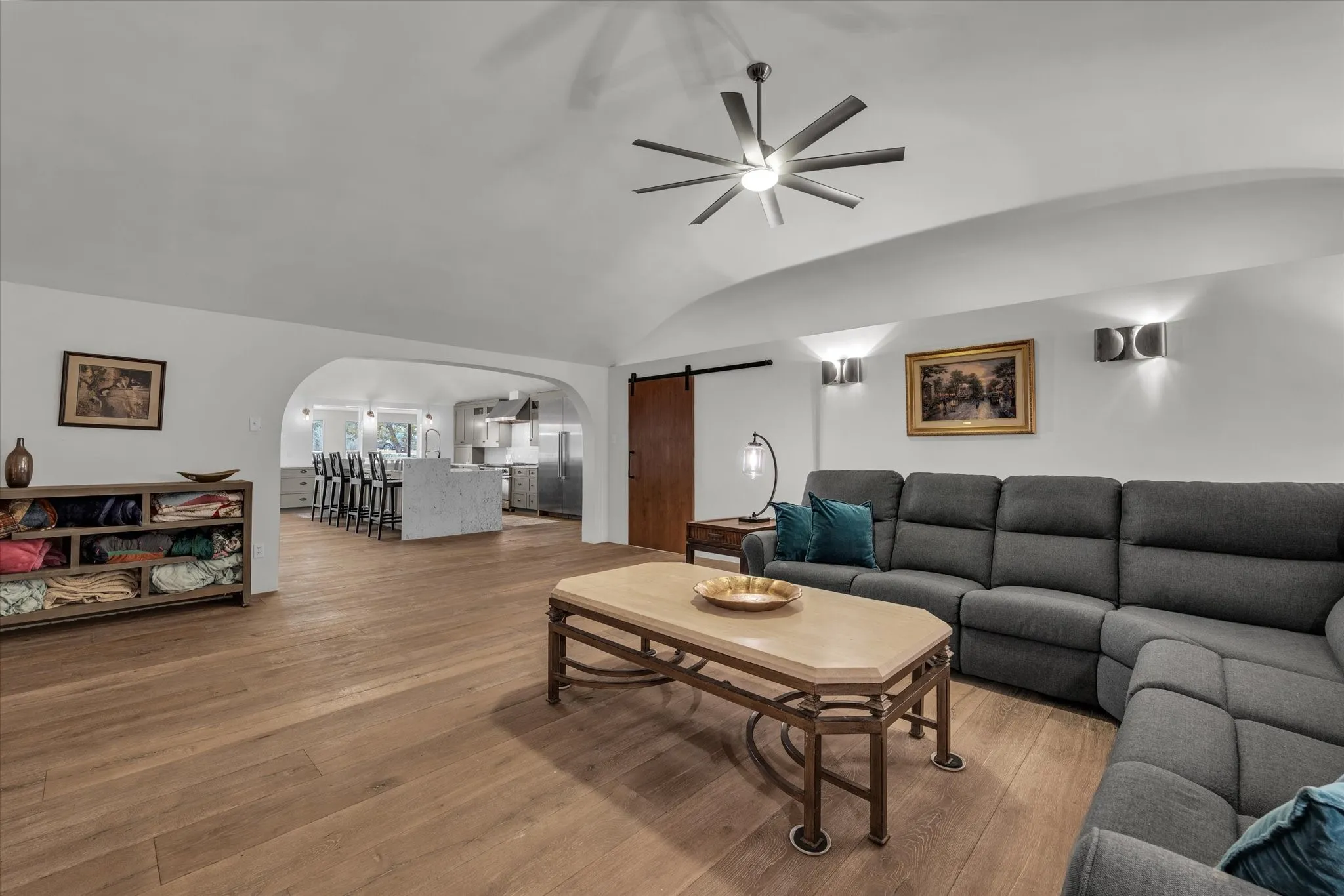 Living room with a barn door, arched walkways, wood-type flooring, and a ceiling fan