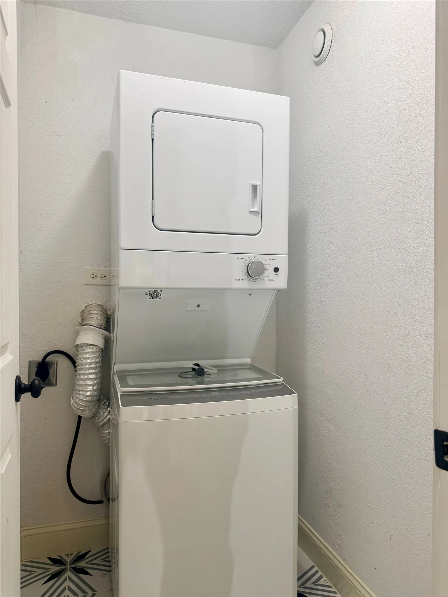 Laundry room with stacked washer / drying machine and a textured wall