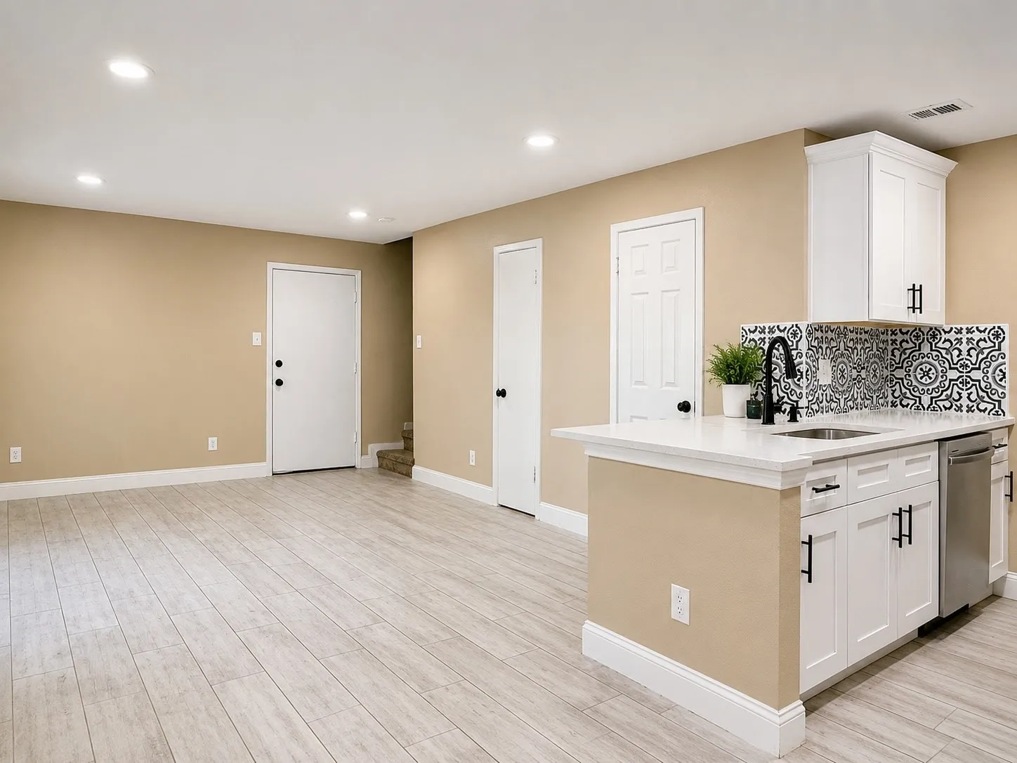 Light wood-finish flooring, recessed lighting, white cabinetry with black hardware, white countertop, and a patterned tile backsplash