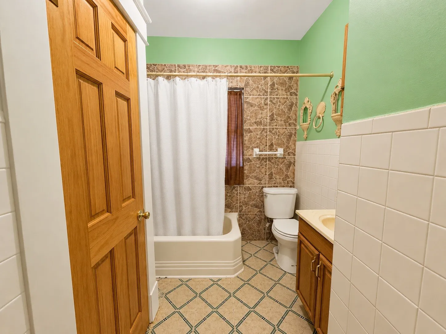 Full bathroom featuring a paneled wood door, a tiled tub surround, a toilet, a vanity with a base cabinet, and patterned floor tiling
