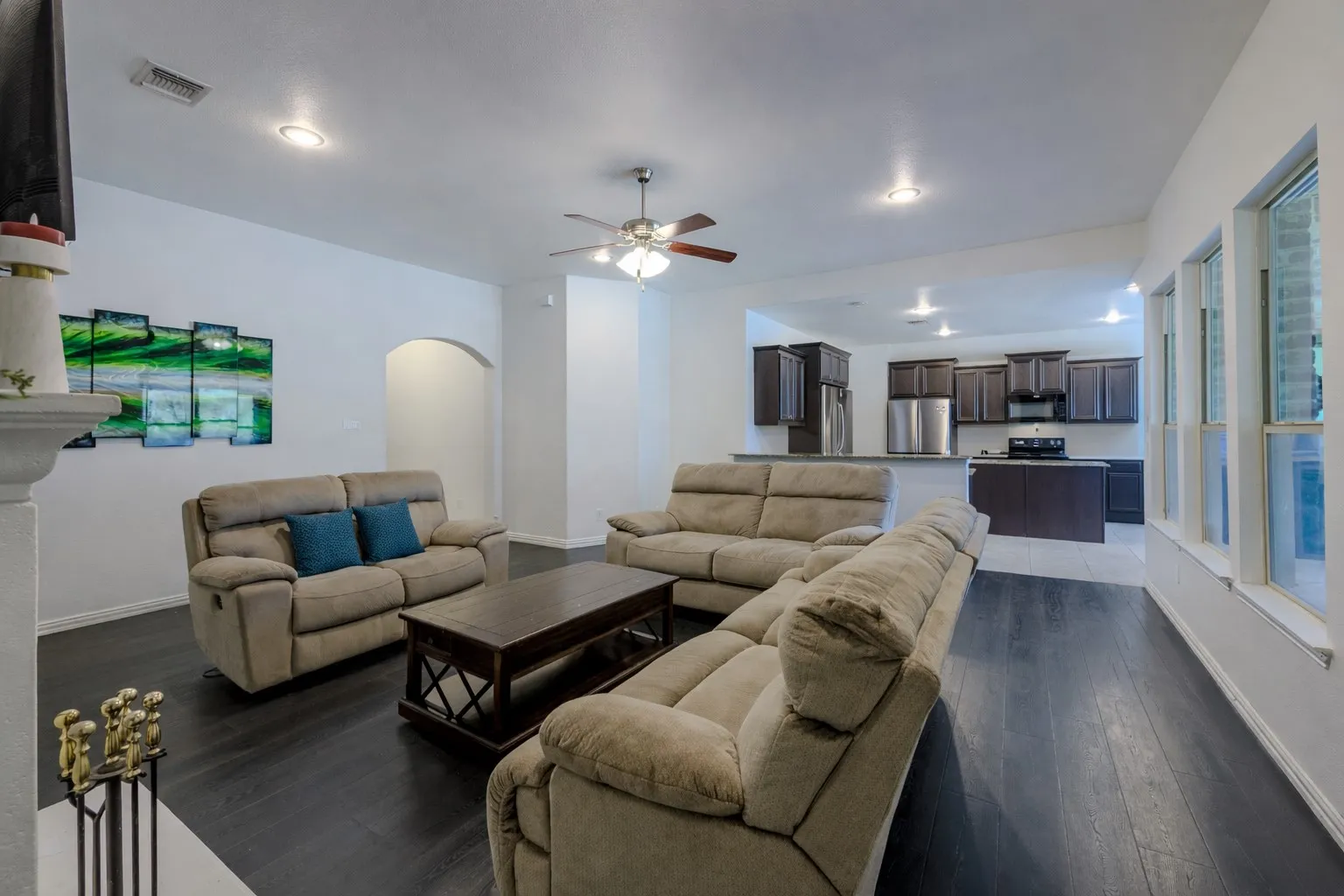 Living room with arched walkways, ceiling fan, dark wood-style flooring, and recessed lighting