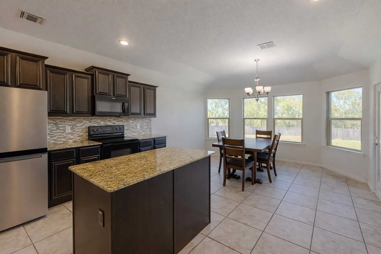 Kitchen featuring dark brown cabinets, black appliances, a chandelier, a center island, and light tile patterned floors
