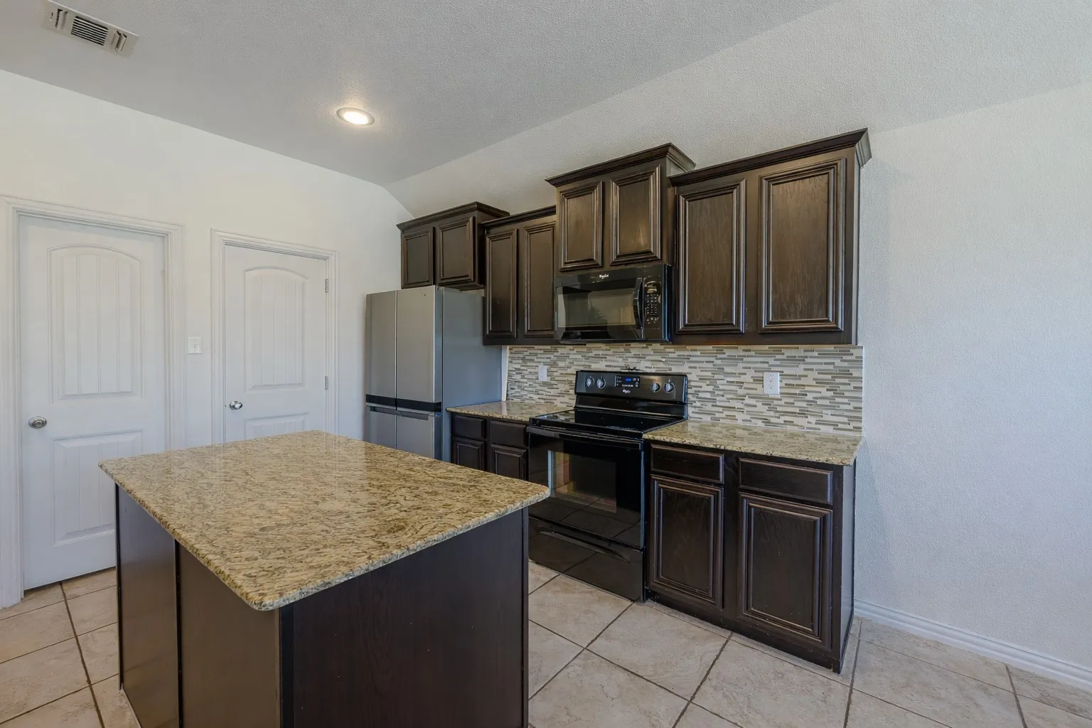 Kitchen featuring dark brown cabinetry, black appliances, a kitchen island, light tile patterned floors, and backsplash