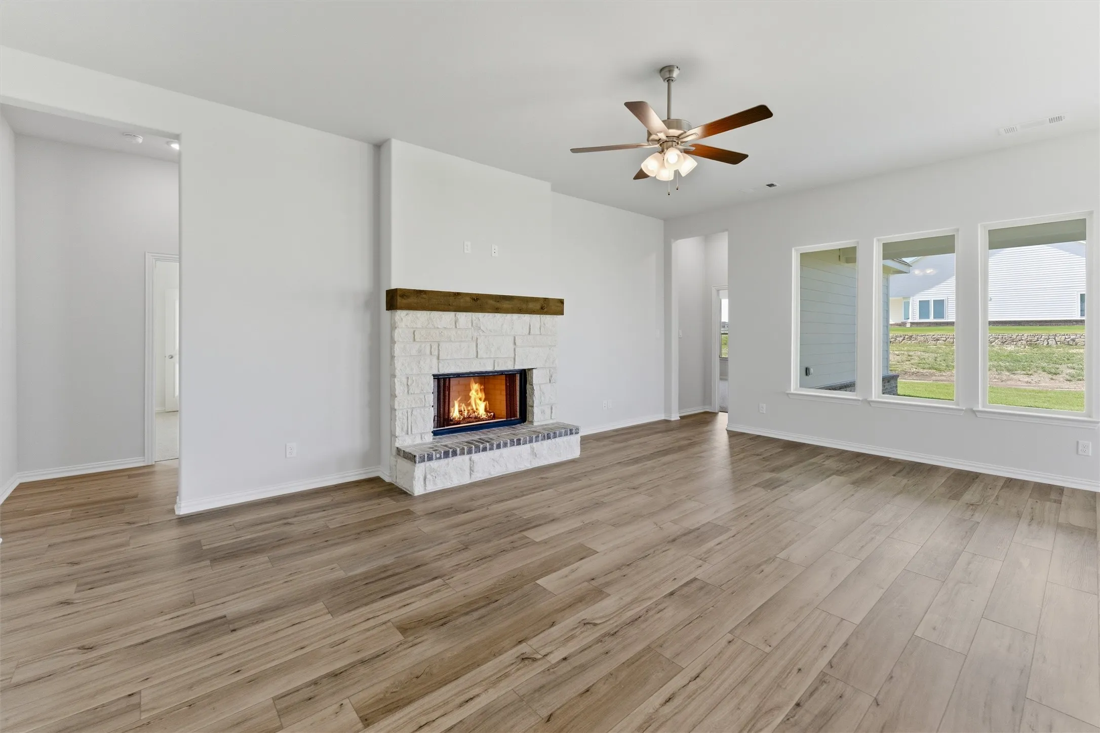 Spacious living area featuring light wood-finish flooring and a stone fireplace with a substantial wood mantel