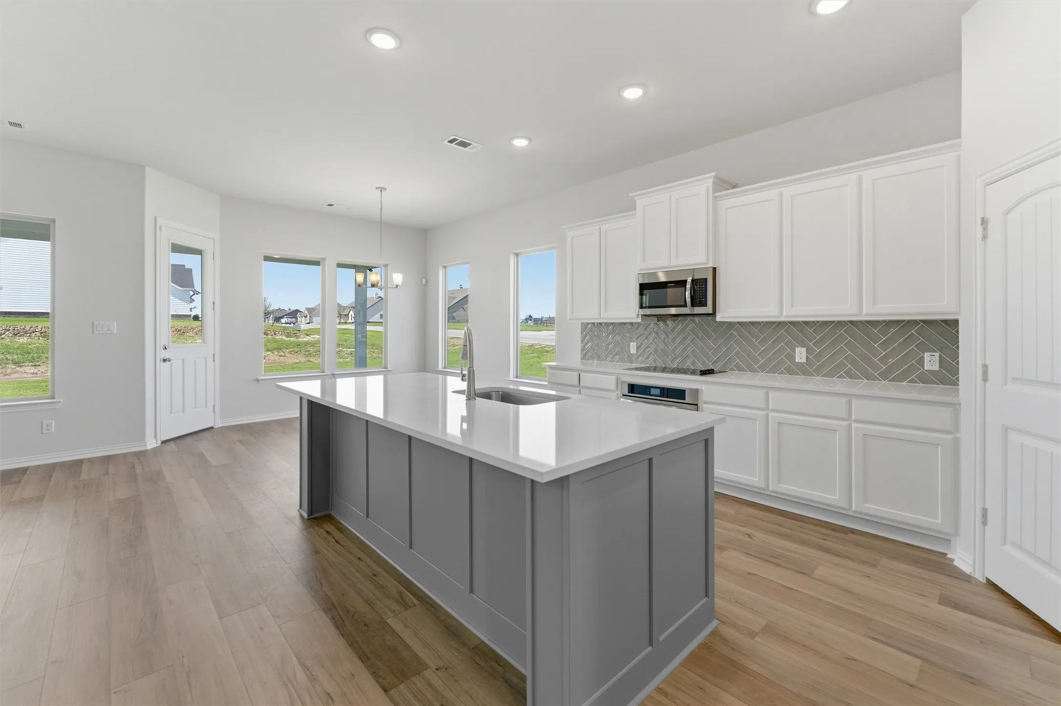 Open-concept kitchen featuring a large island with a sink, white cabinetry, integrated stainless steel appliances, a herringbone tile backsplash, and light wood-finish flooring