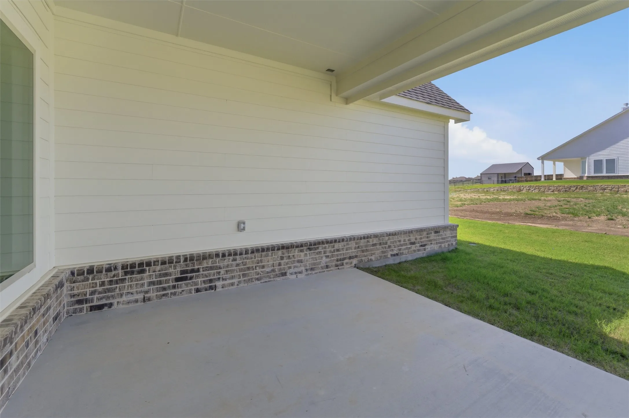Covered concrete patio with white horizontal siding and a brick skirting