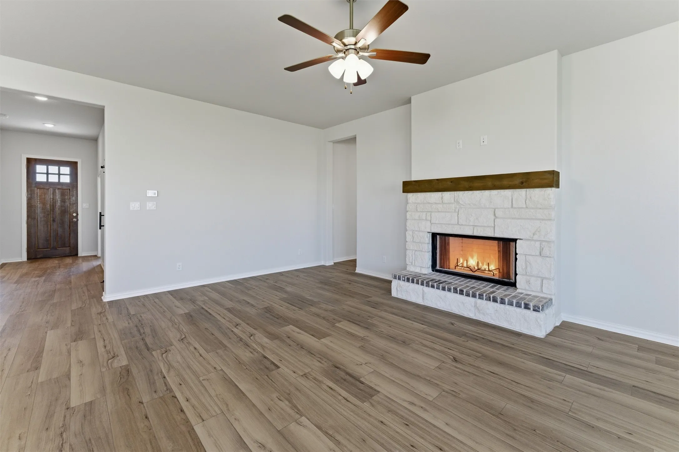 Spacious living area featuring wood-finish flooring, a white stone fireplace with a dark wood mantel, and a ceiling fan with integrated lighting