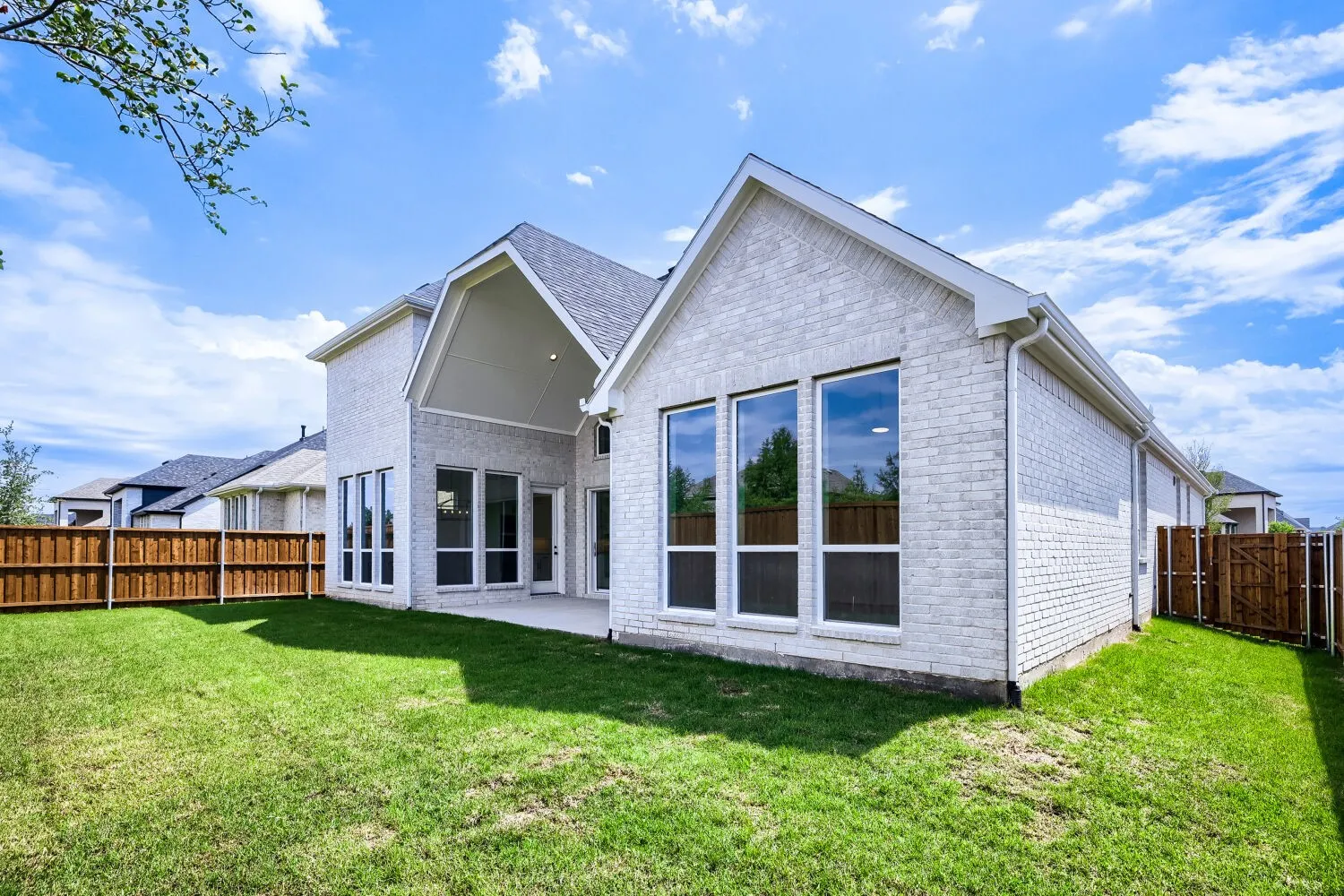 Spacious backyard featuring a manicured lawn, a light-colored brick exterior, a covered patio, and large windows