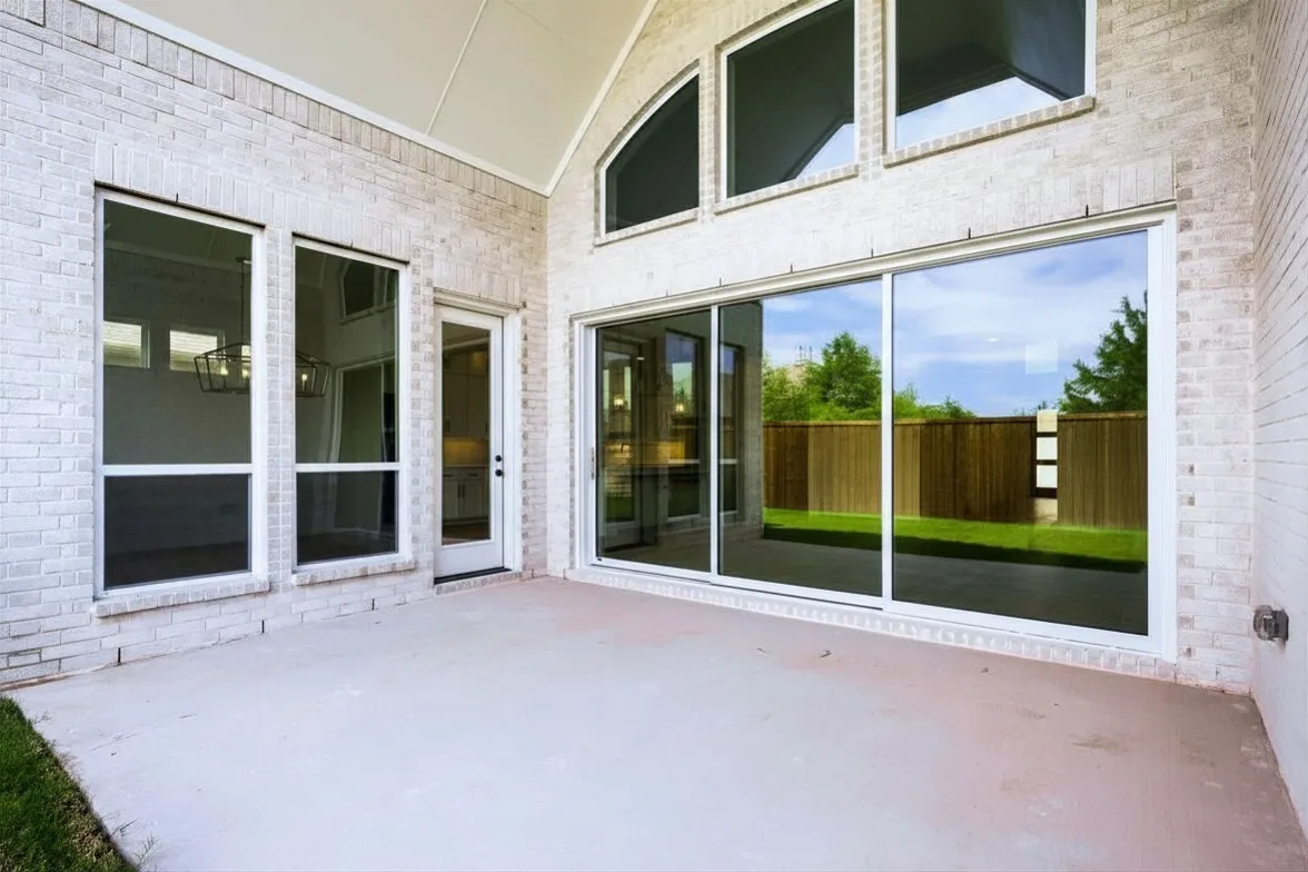 Covered patio with a concrete surface, white brick exterior, large sliding glass doors, a single glass panel door, and multiple tall windows
