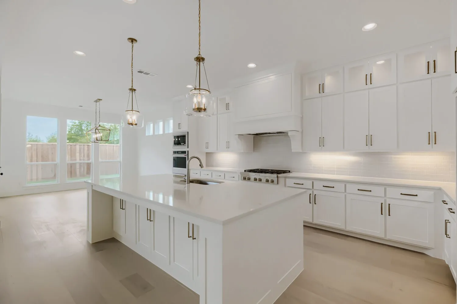 Spacious kitchen featuring an expansive island with a sink, white cabinetry with gold-toned hardware, stainless steel appliances including a built-in oven and gas range, and wood-finish flooring