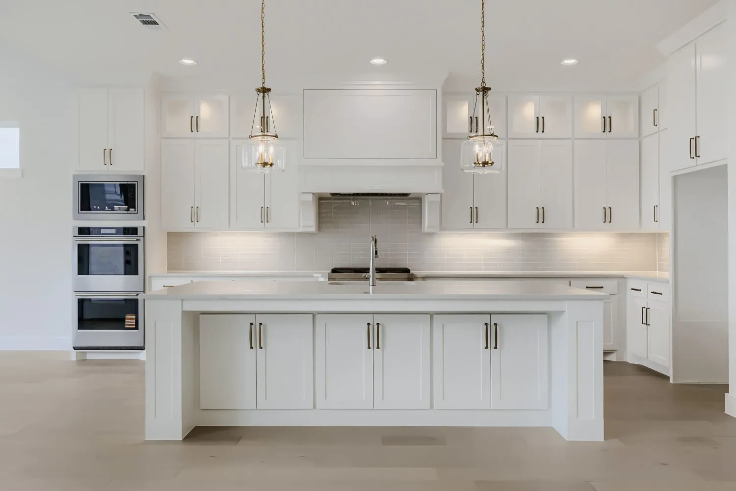 Bright kitchen featuring an expansive center island, white shaker cabinetry, stainless steel appliances, a subway tile backsplash, and recessed and pendant lighting