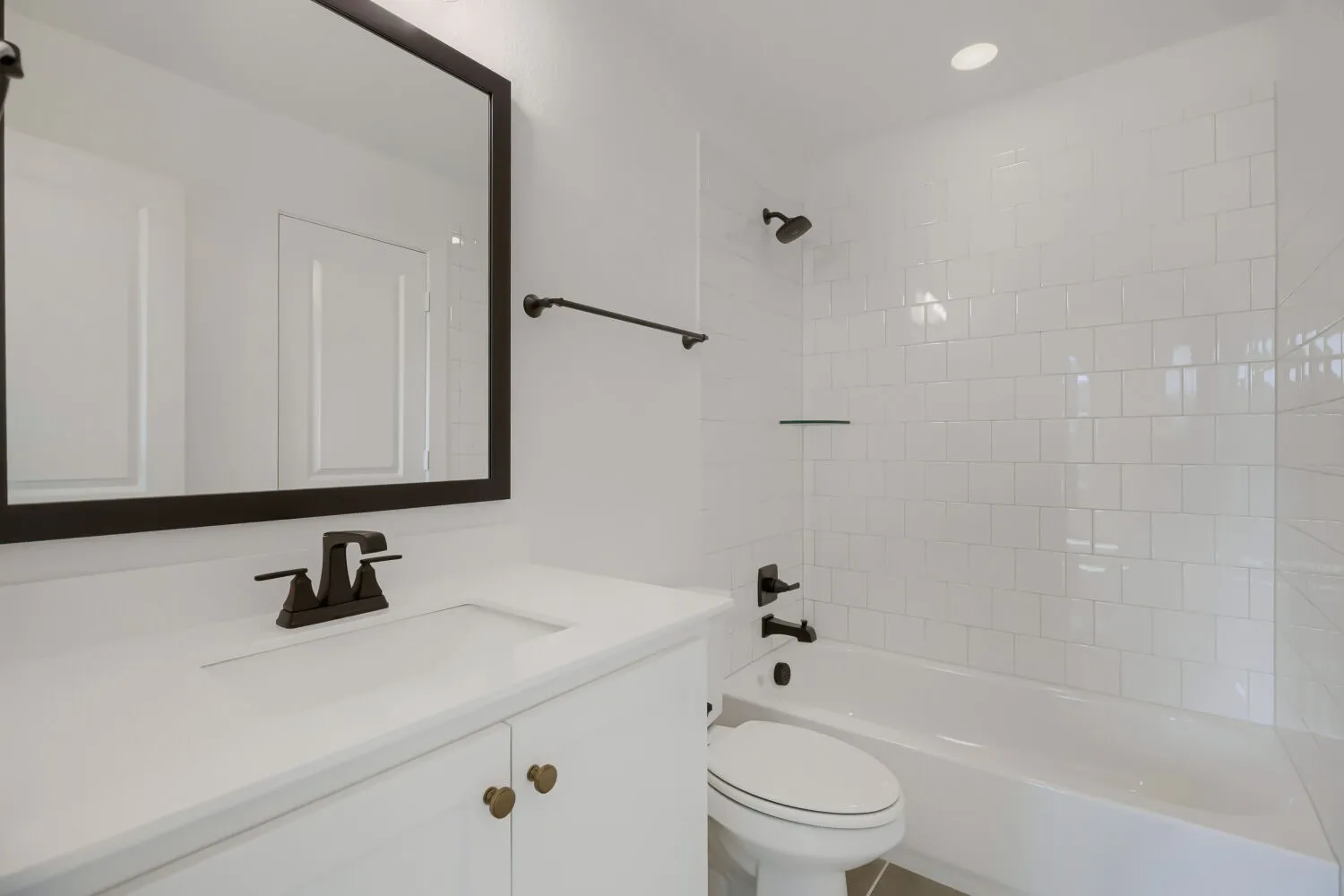 White vanity with integrated sink and dark bronze fixtures, framed mirror, and recessed lighting