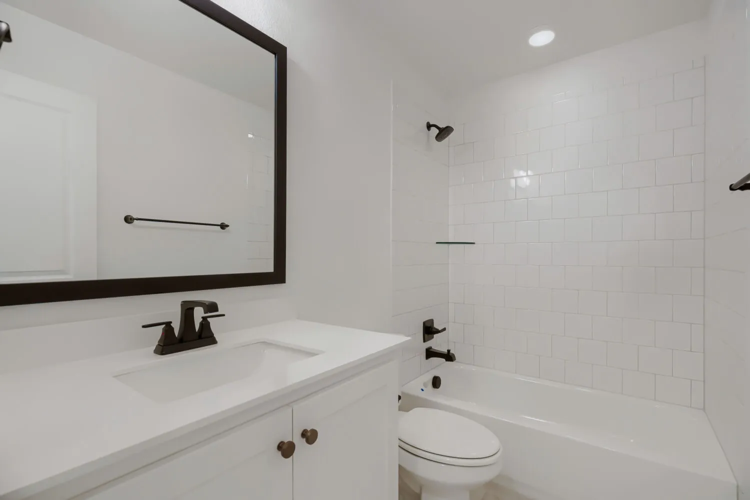 Bright bathroom featuring a white vanity with integrated sink, a dark-framed mirror, and matte black fixtures