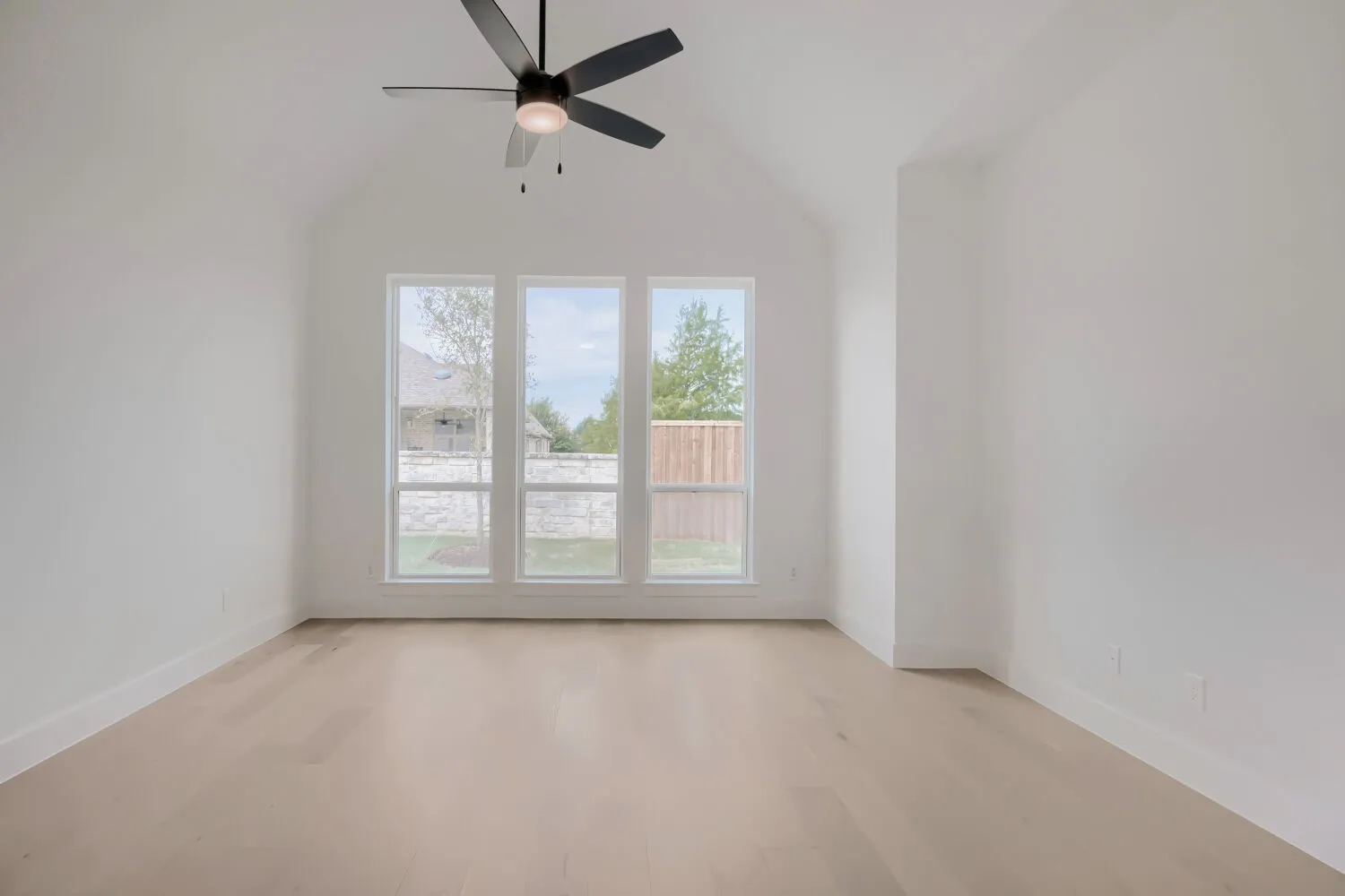 Vaulted ceiling room featuring three large windows, a ceiling fan with integrated lighting, wood-finish flooring, and white baseboards