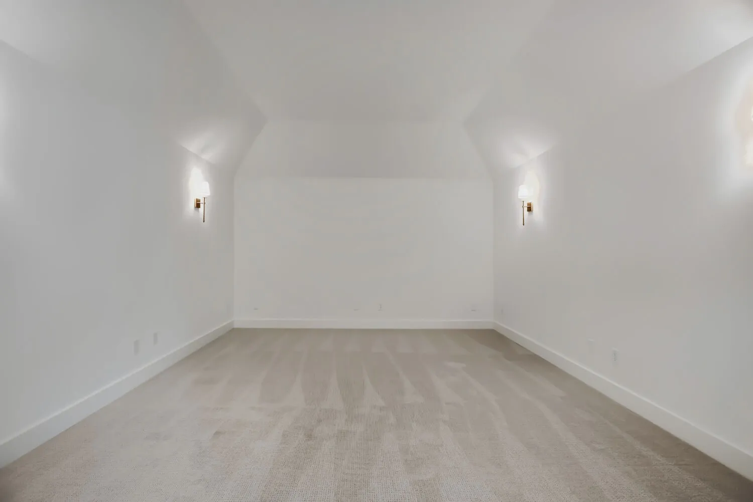 Spacious room featuring neutral carpeting, crisp white walls, and elegant sconce lighting