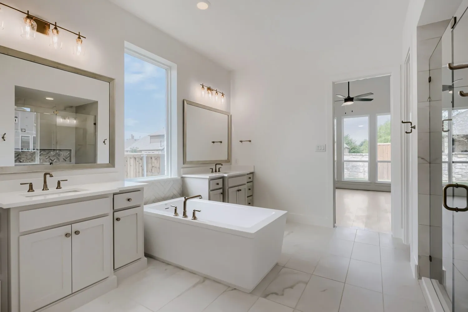 Freestanding soaking tub with floor-mounted faucet, dual vanity with undermount sinks, separate glass-enclosed shower, expansive window, and tile flooring