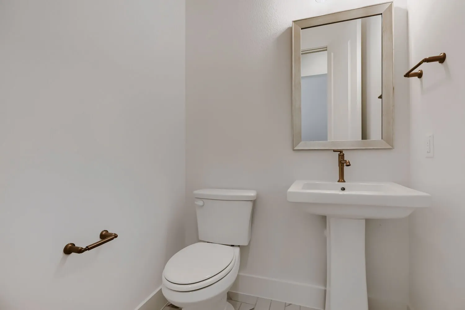 Pedestal sink with a bronze-finish faucet, framed mirror, and coordinating bronze-finish towel bar