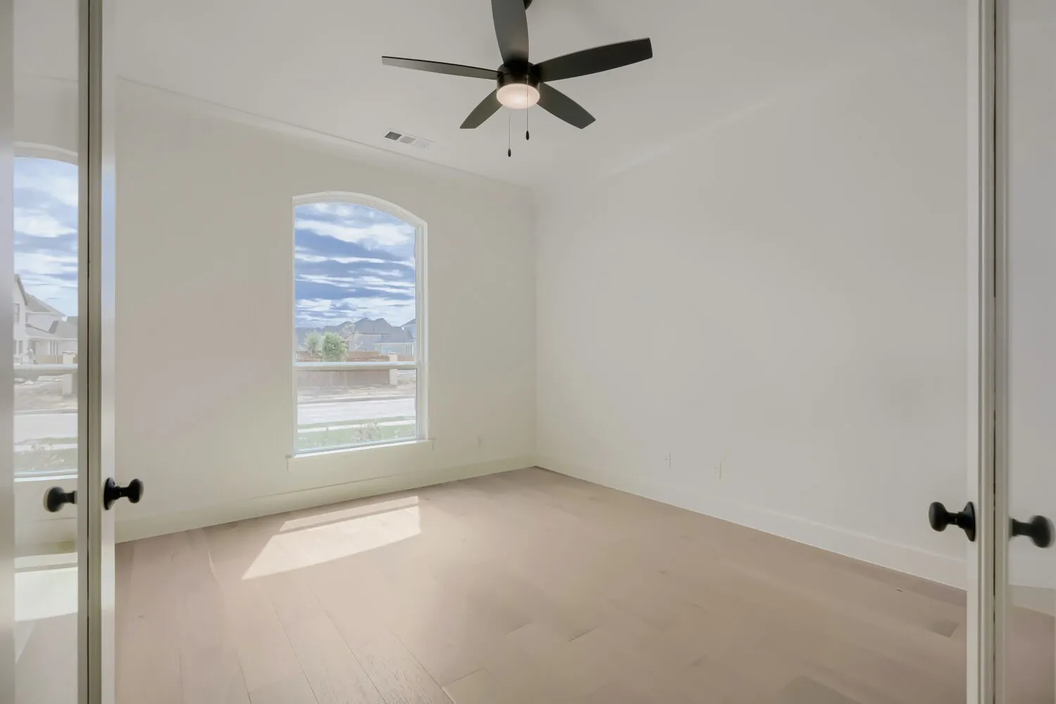 Light wood-finish flooring with a contemporary black ceiling fan and light fixture