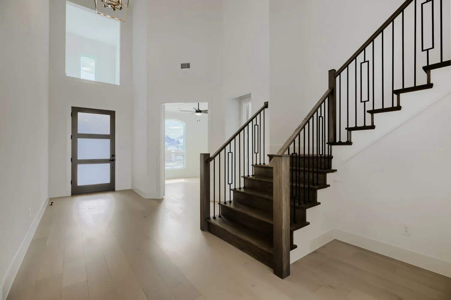 Double-height entry featuring a prominent staircase with dark wood-finish treads and risers, black metal balusters, and a matching handrail