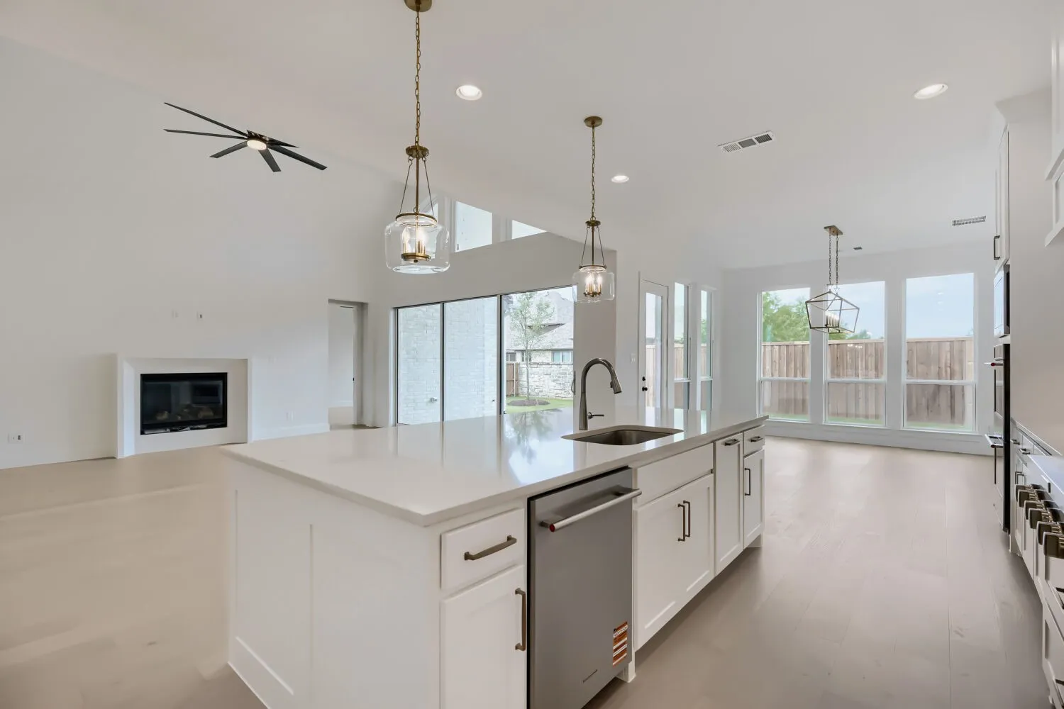 Spacious open-concept kitchen featuring a large central island with a built-in sink and dishwasher, white cabinetry, and a light-toned countertop