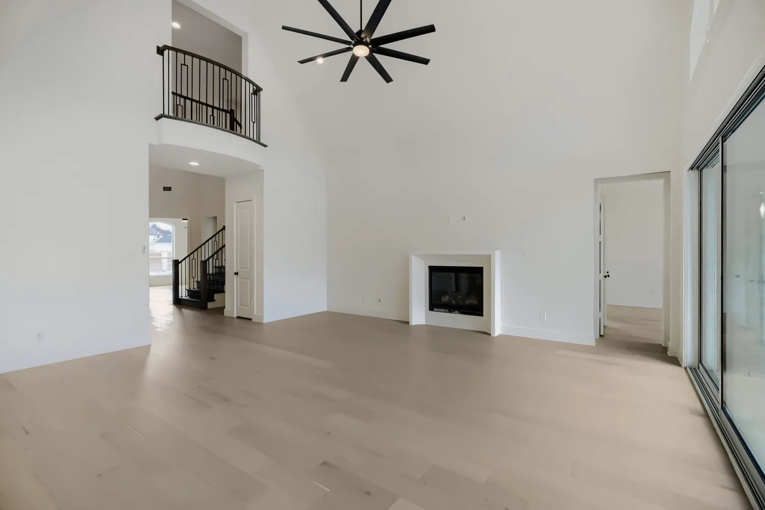 Spacious living area featuring high vaulted ceilings, light wood-finish flooring, and a modern fireplace with a white surround