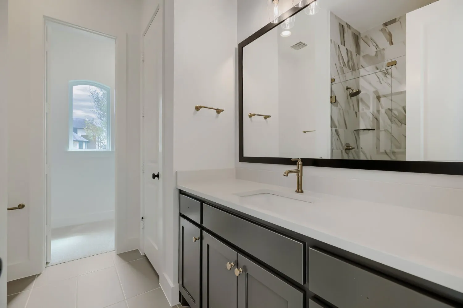 Bathroom featuring a gray vanity with a light-toned countertop, a large framed mirror, and a walk-in shower with large format tile