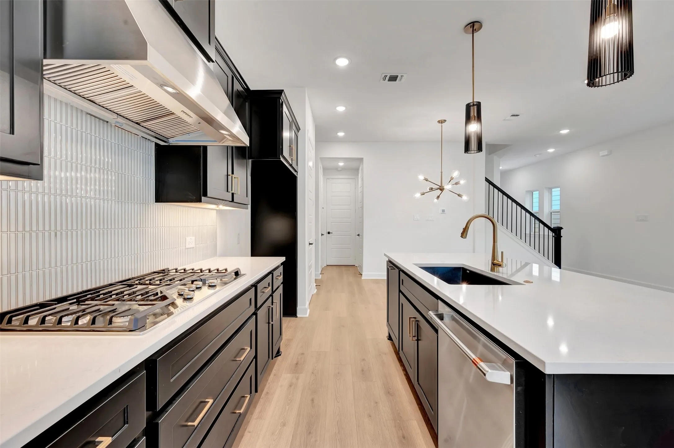 Modern kitchen featuring dark cabinetry, light wood-finish flooring, white countertops, and a white vertical tile backsplash