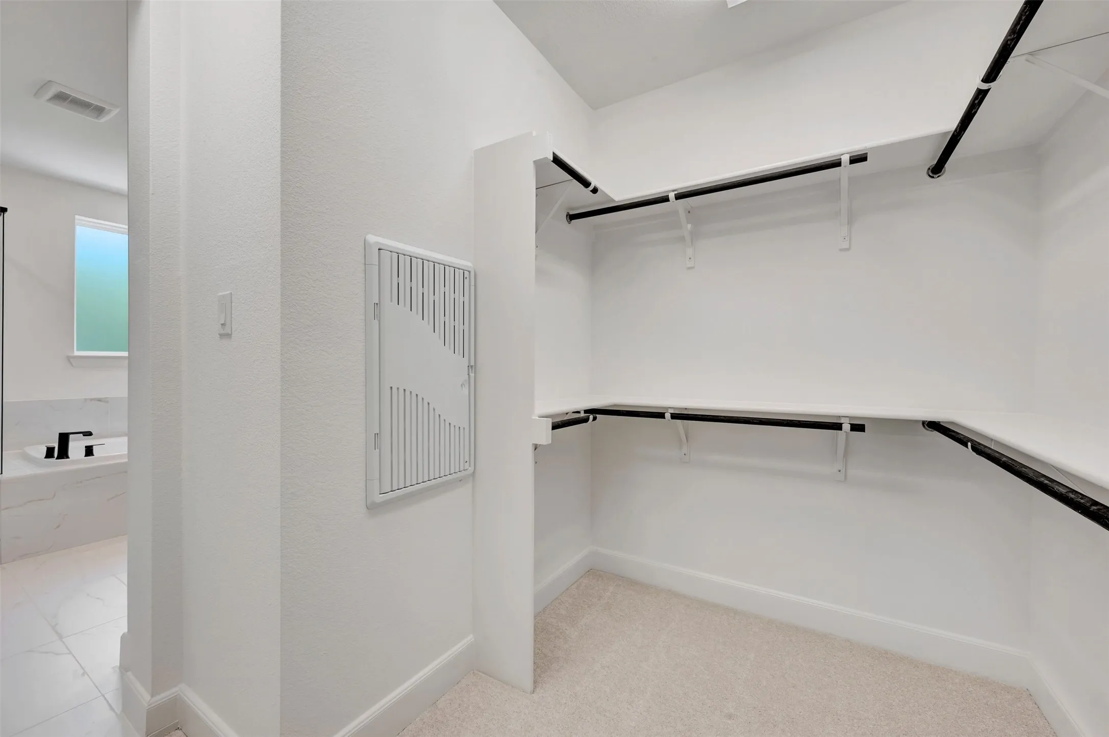 Spacious walk-in closet featuring white walls, multi-level shelving, black clothing rods, and light-colored carpet flooring