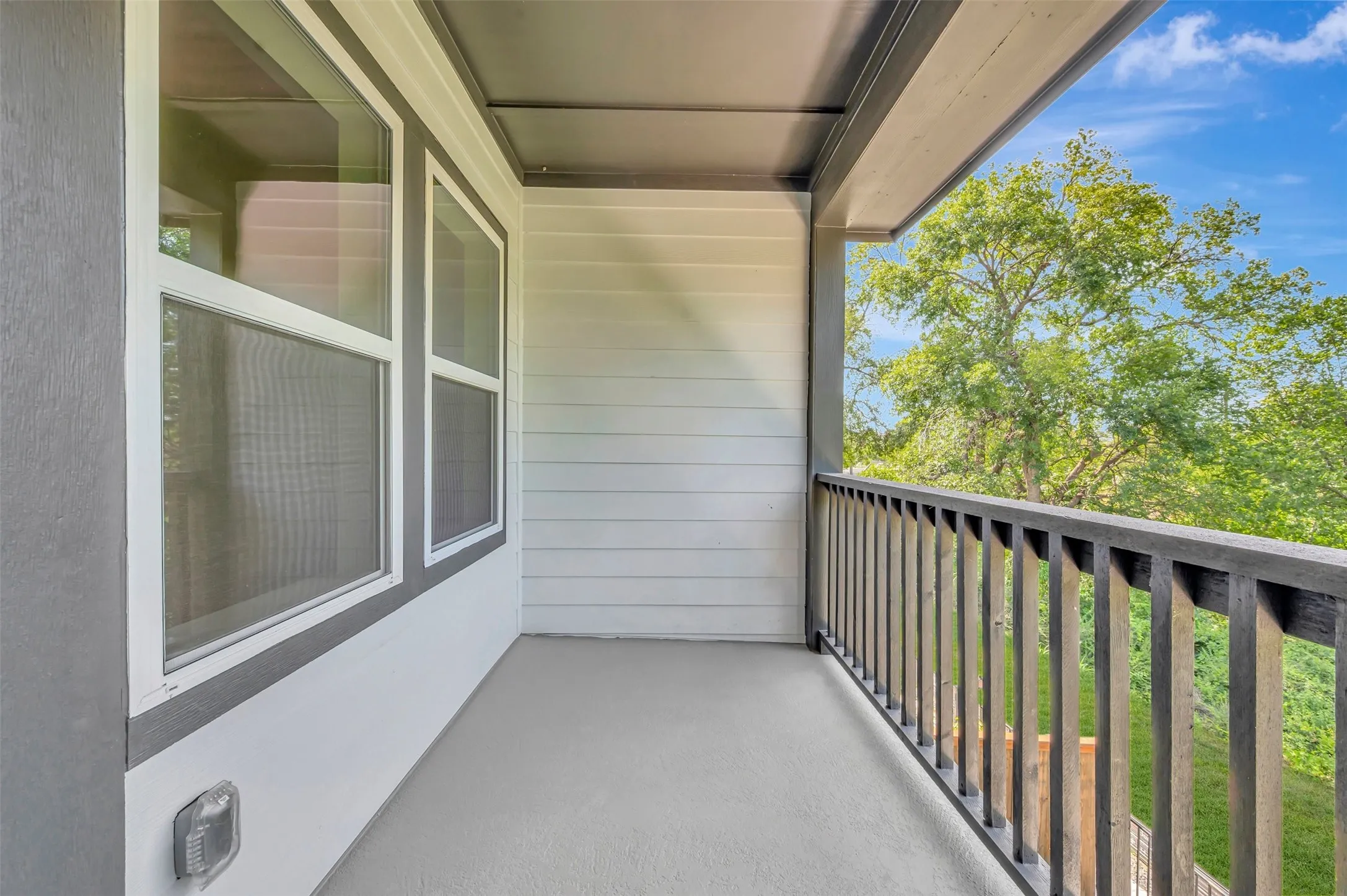 Covered outdoor balcony with a neutral gray floor, dark wood railing, and white horizontal siding