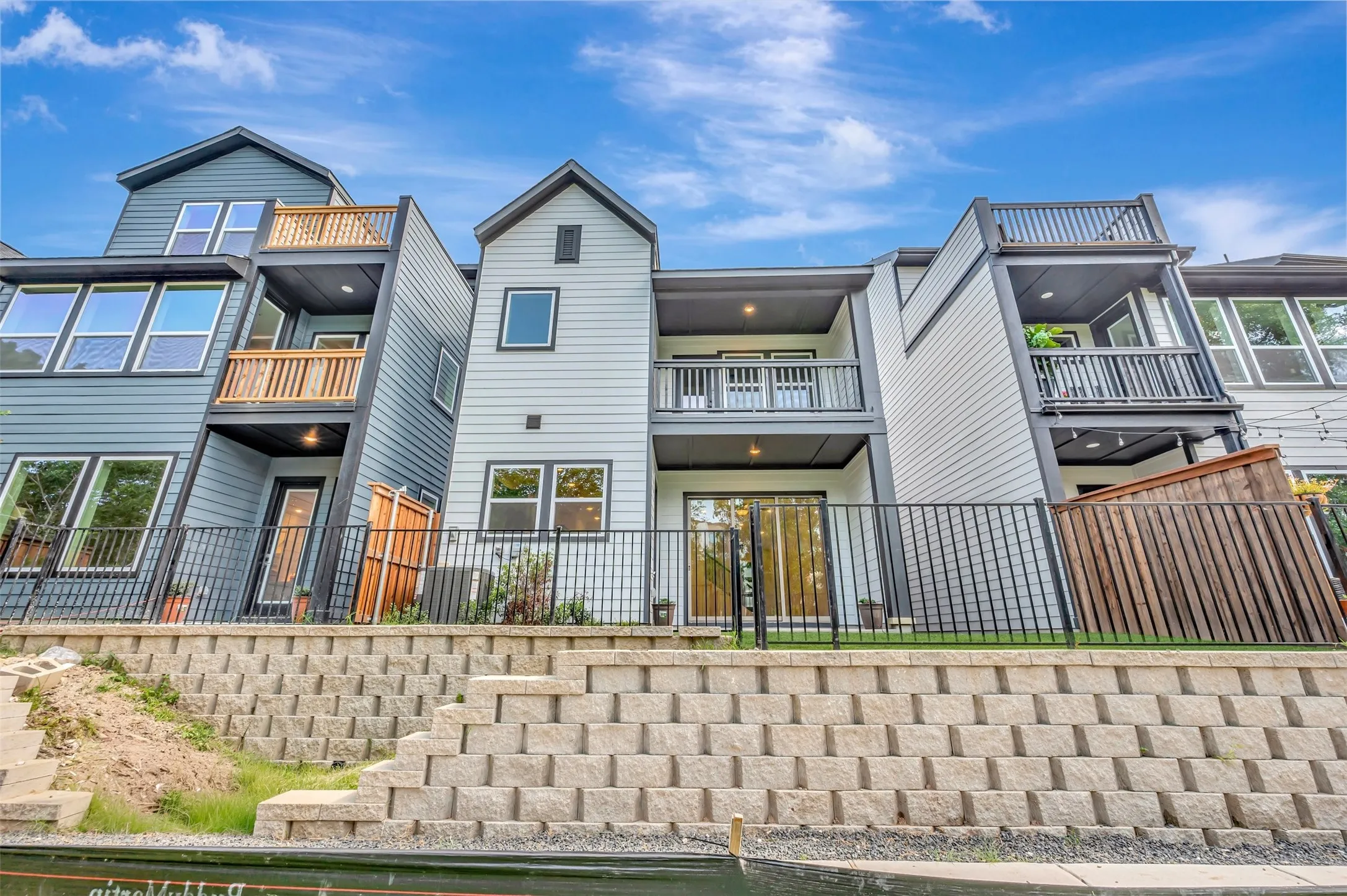 Contemporary multi-level exterior featuring light-colored siding, multiple balconies with dark railings, and a ground-level patio with sliding glass doors