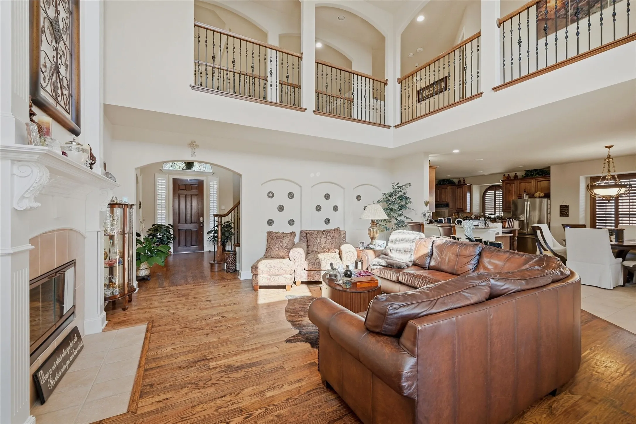 Living room featuring arched walkways, a tile fireplace, light wood finished floors, stairway, and a high ceiling