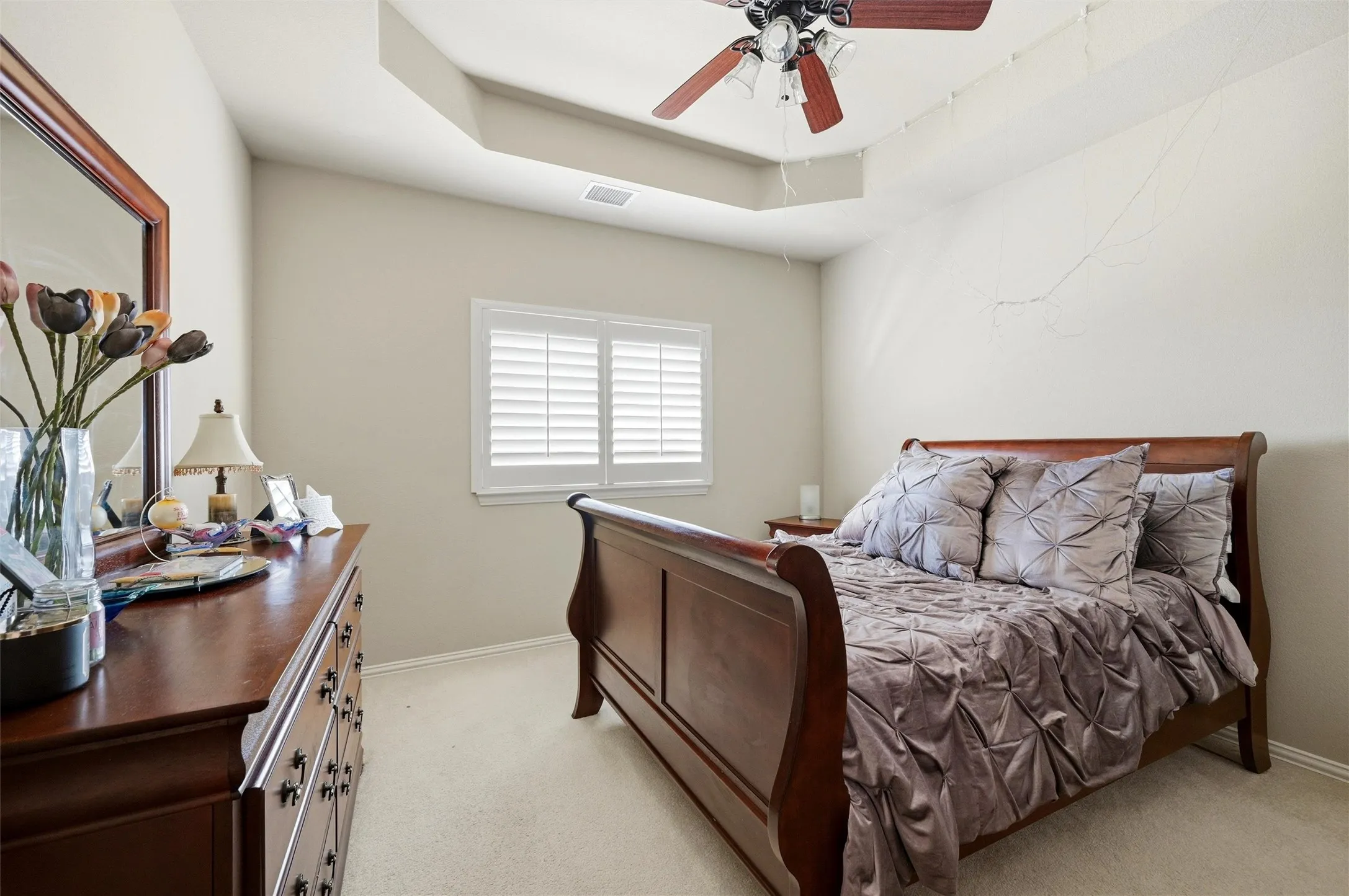 Bedroom with a raised ceiling, light colored carpet, and a ceiling fan