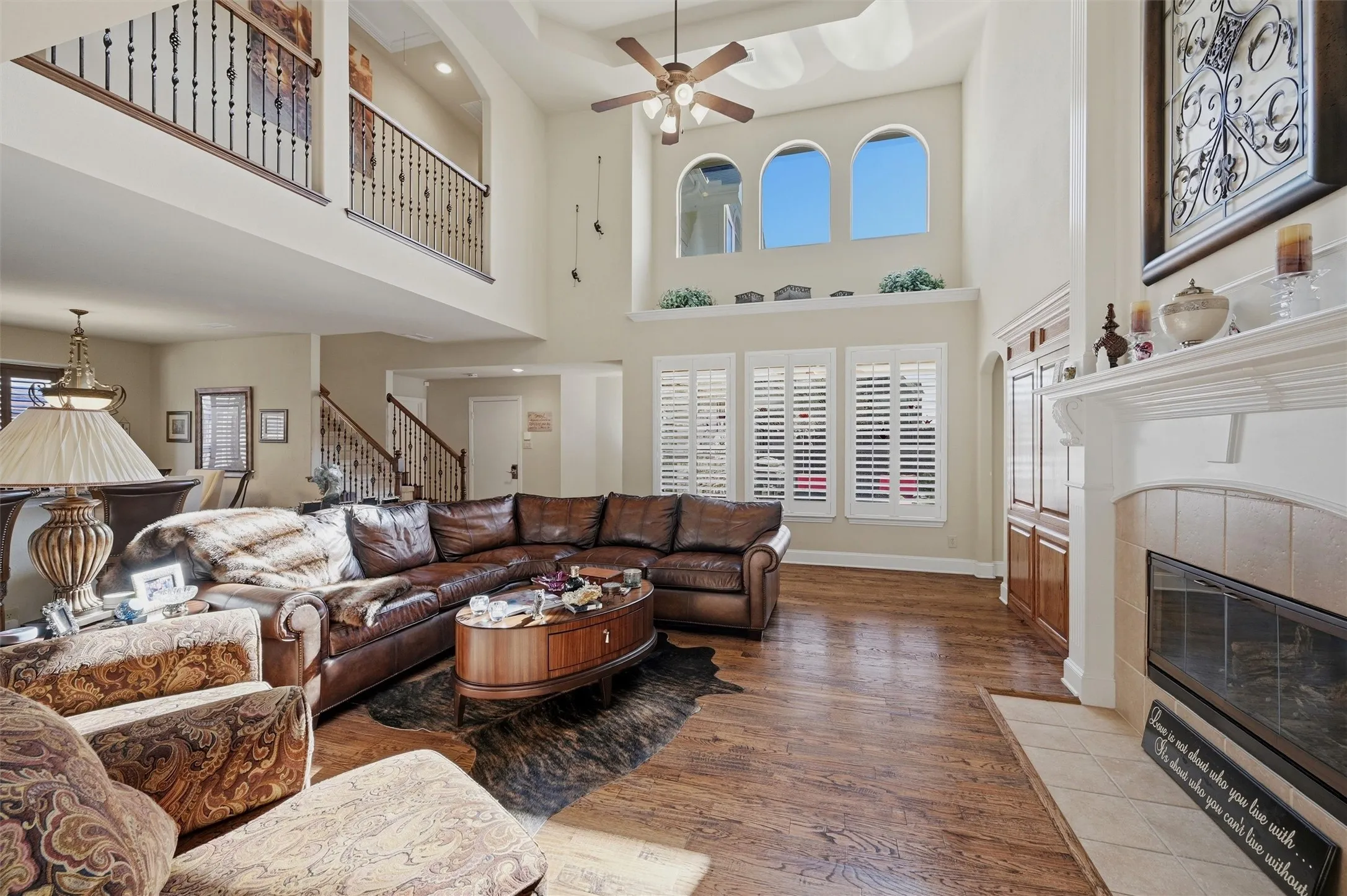 Living room featuring a fireplace, wood finished floors, a high ceiling, ceiling fan, and stairs