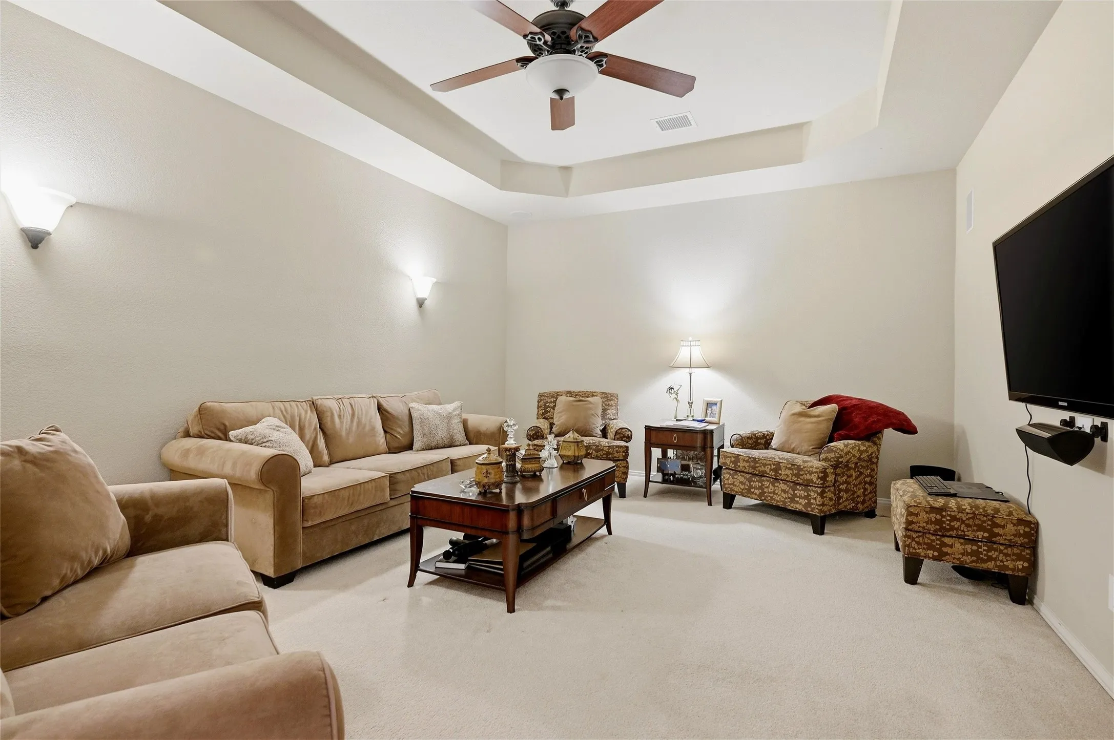 Living room featuring a raised ceiling, carpet flooring, and ceiling fan