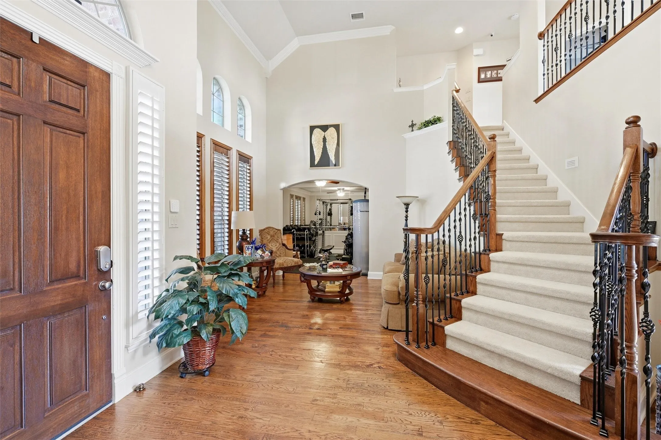 Foyer featuring arched walkways, crown molding, wood finished floors, a high ceiling, and stairway