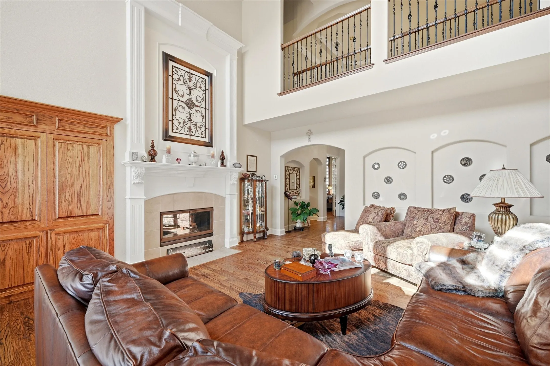 Living area with a towering ceiling, arched walkways, a tile fireplace, and wood finished floors