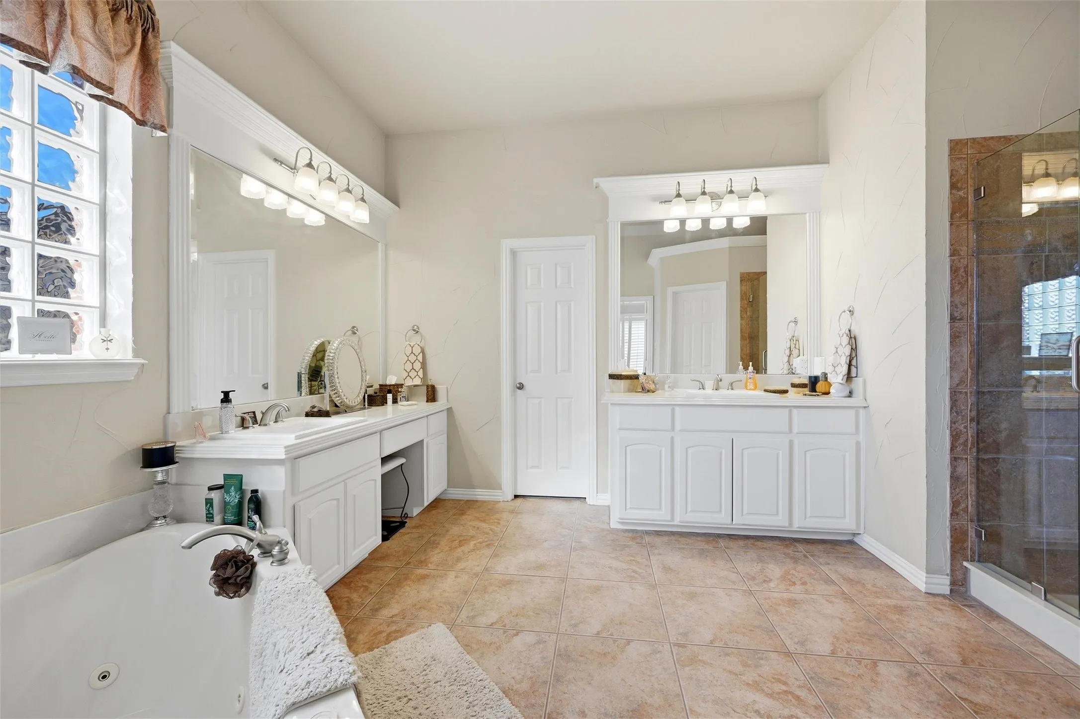 Full bath featuring two vanities, a shower stall, a tub with jets, and plenty of natural light
