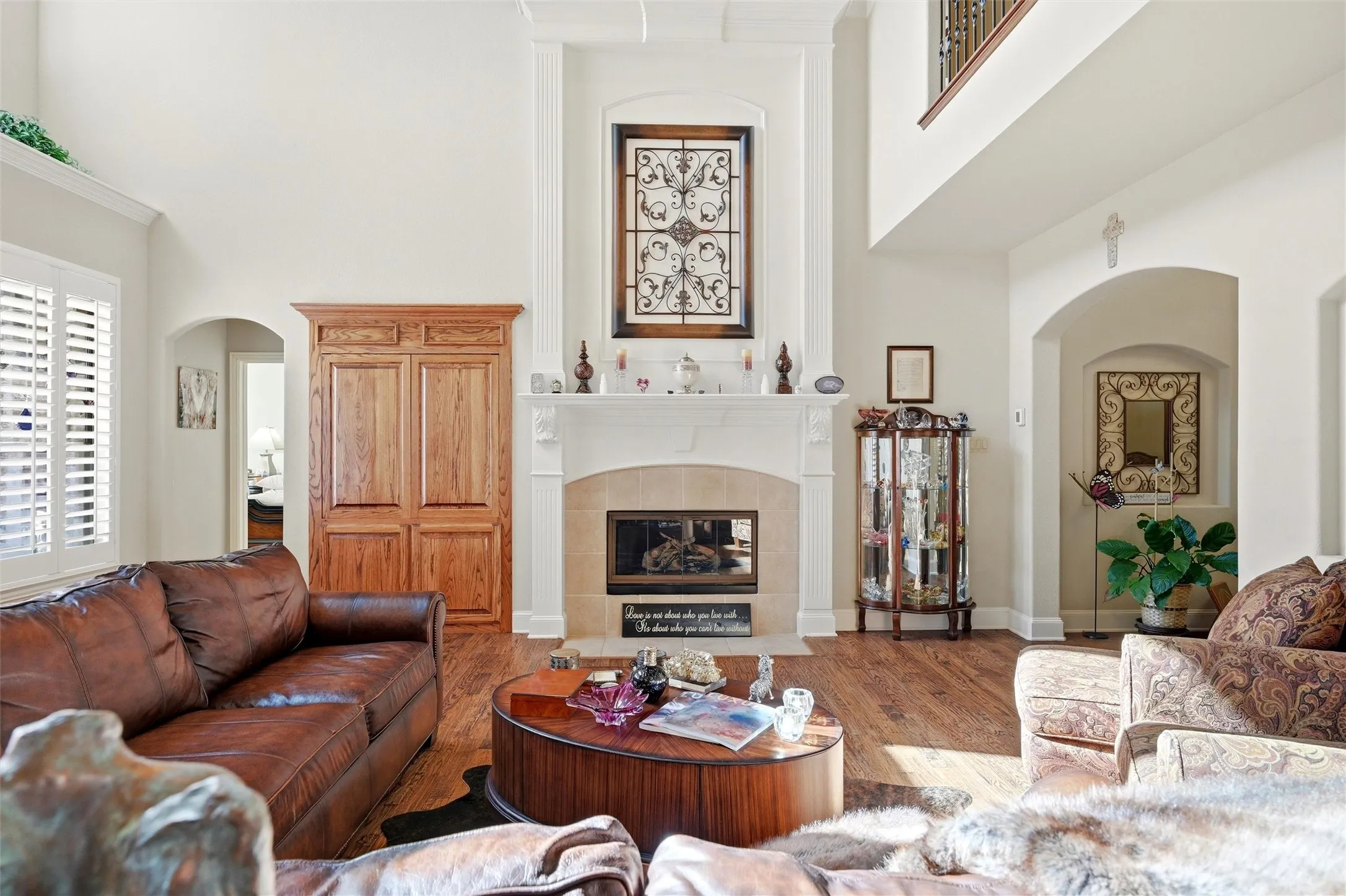 Living room with a high ceiling, a tile fireplace, arched walkways, and wood finished floors