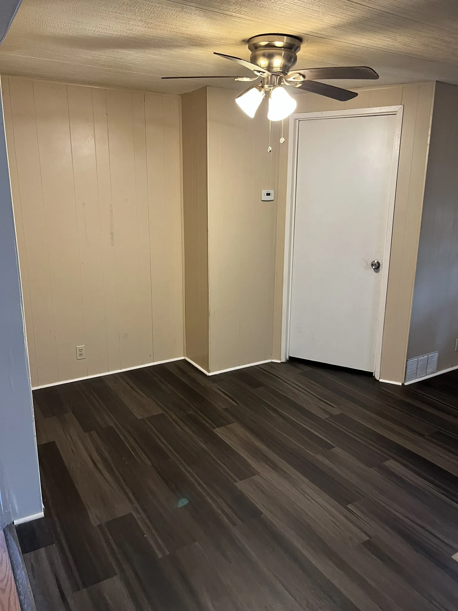 Spare room featuring dark wood-type flooring, wooden walls, and a ceiling fan