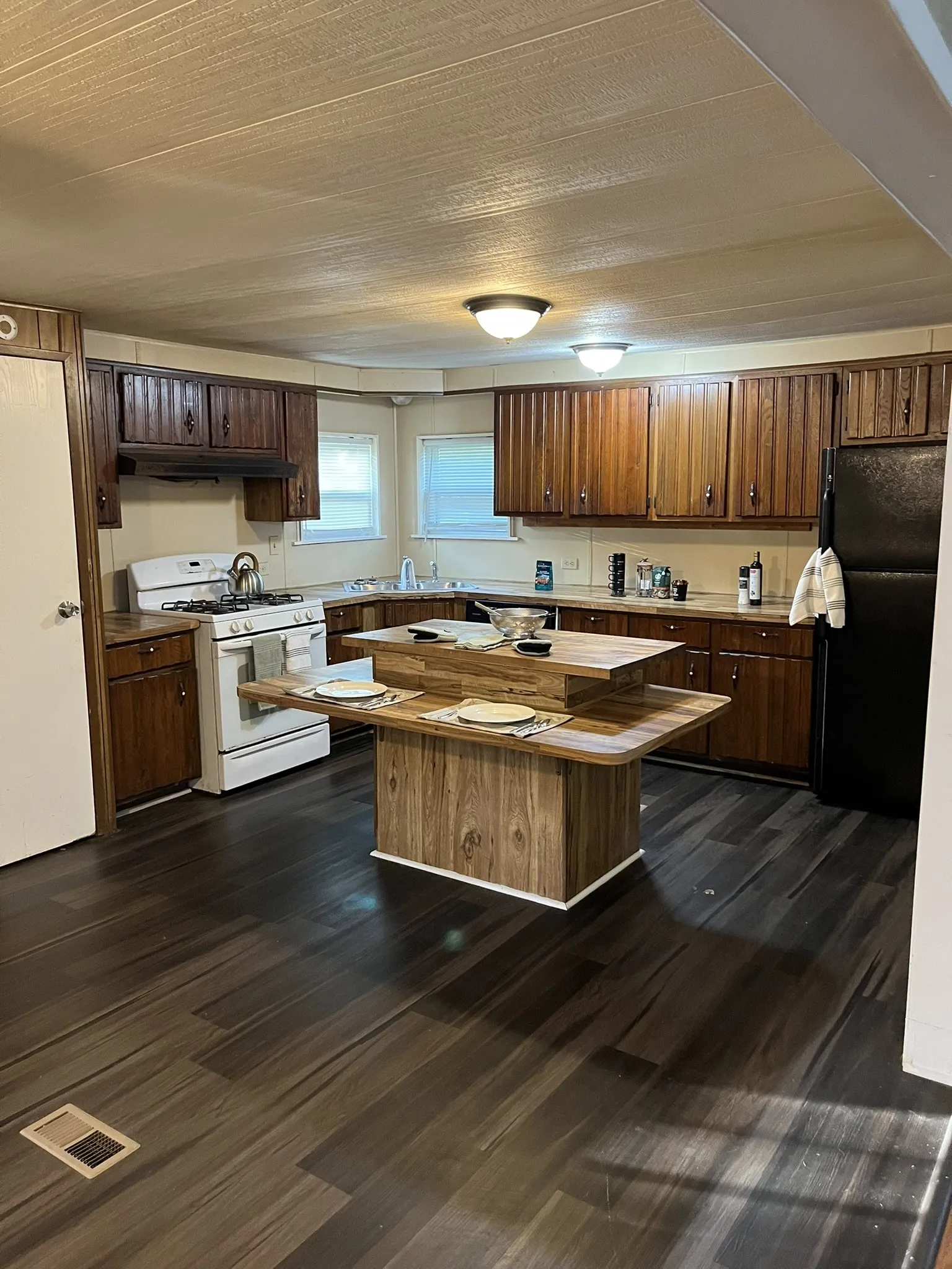 Kitchen featuring white range with gas stovetop, freestanding refrigerator, a kitchen island, dark wood-style floors, and under cabinet range hood