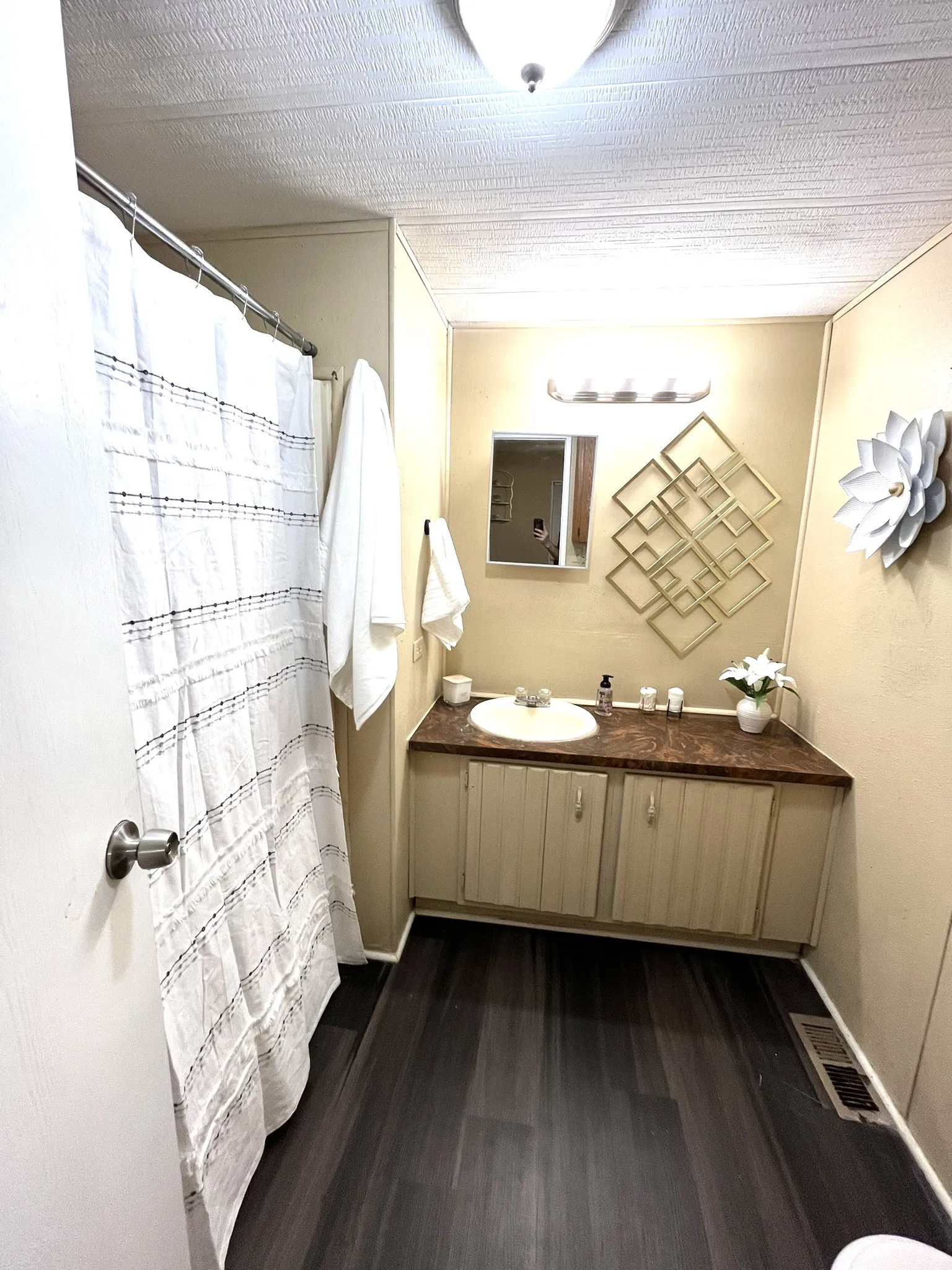 Full bathroom with curtained shower, vanity, dark wood finished floors, and a textured ceiling