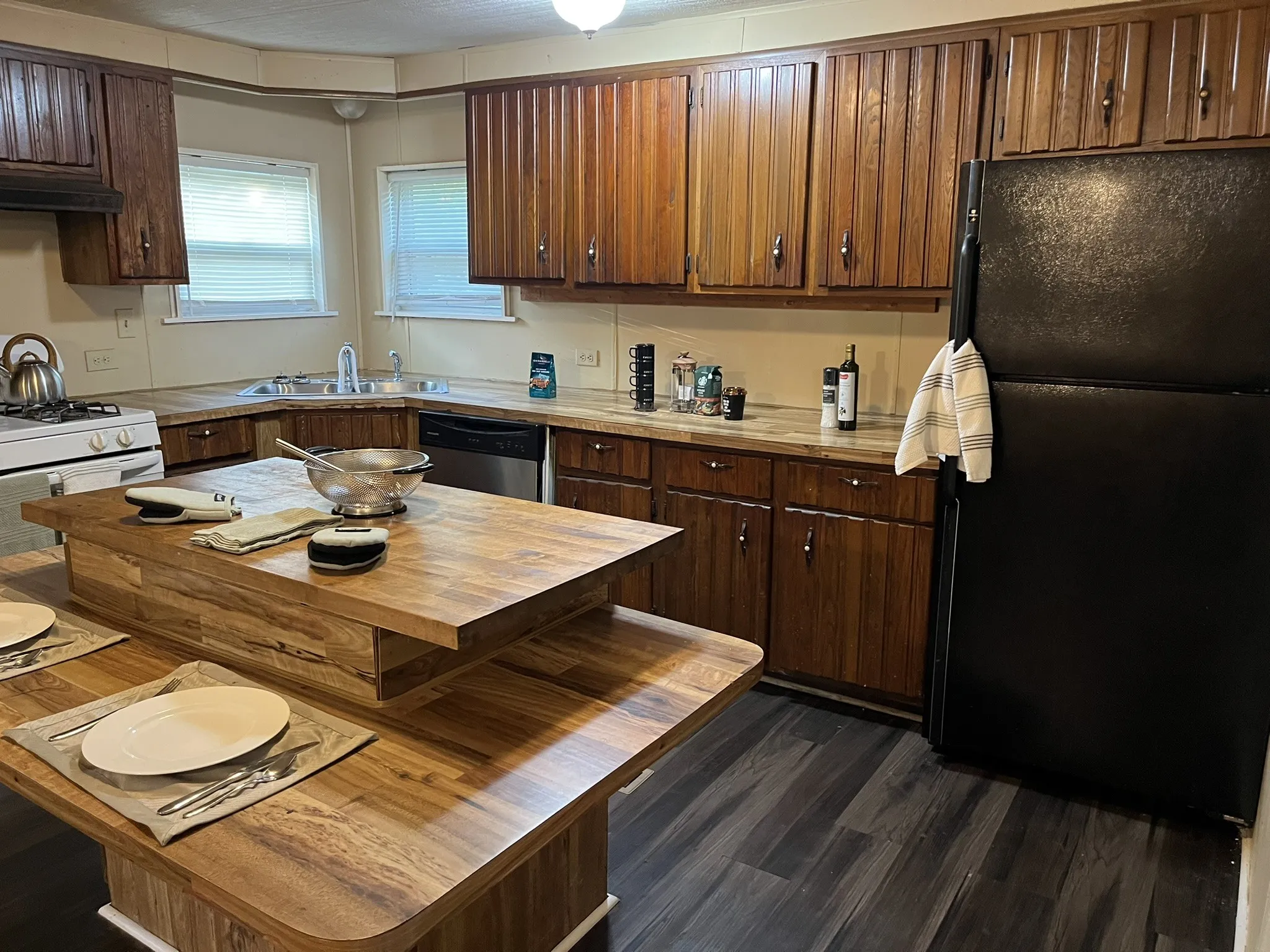 Kitchen with freestanding refrigerator, butcher block countertops, stainless steel dishwasher, dark brown cabinets, and dark wood-type flooring