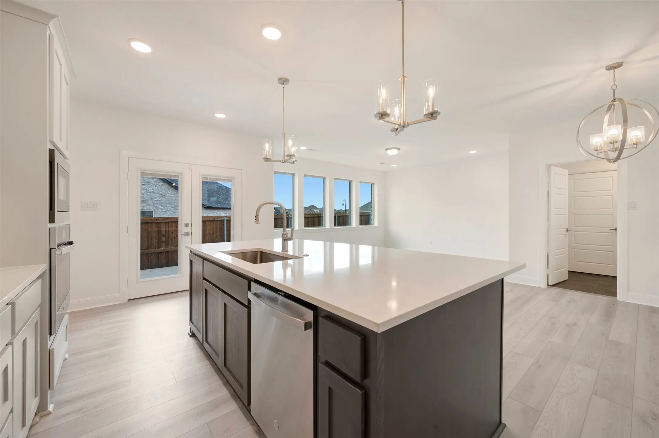 Spacious kitchen featuring a large island with sink, stainless steel dishwasher, modern pendant lighting, white cabinetry, and light wood-finish flooring
