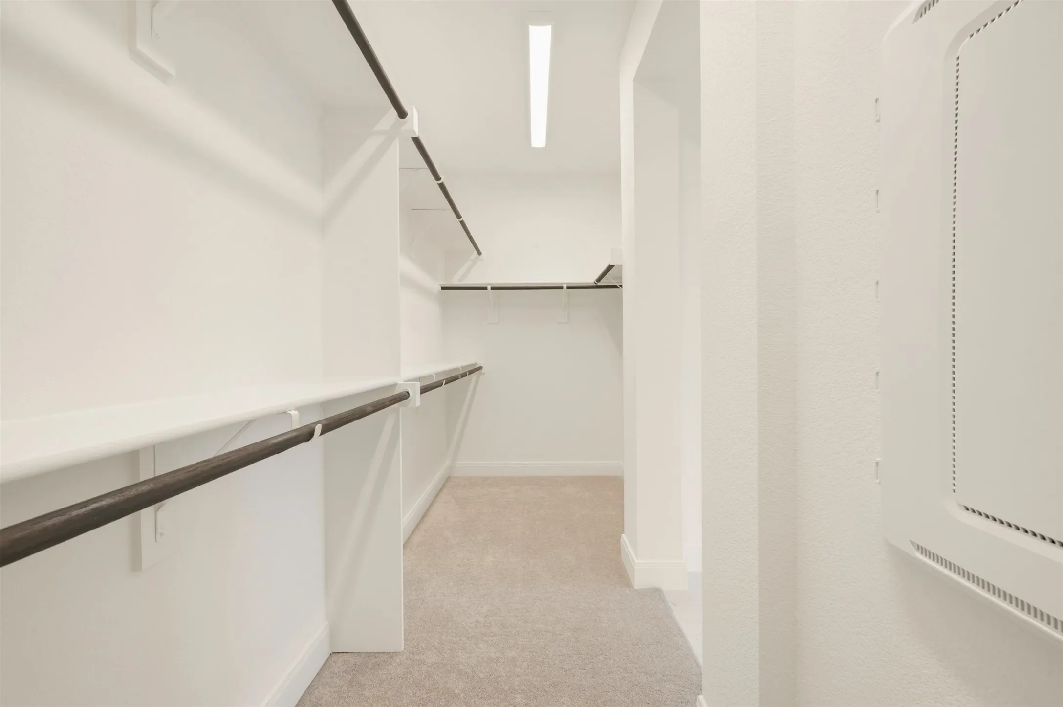 Expansive walk-in closet featuring light beige carpet, multiple levels of white shelving, dark wood-finish hanging rods, and recessed lighting