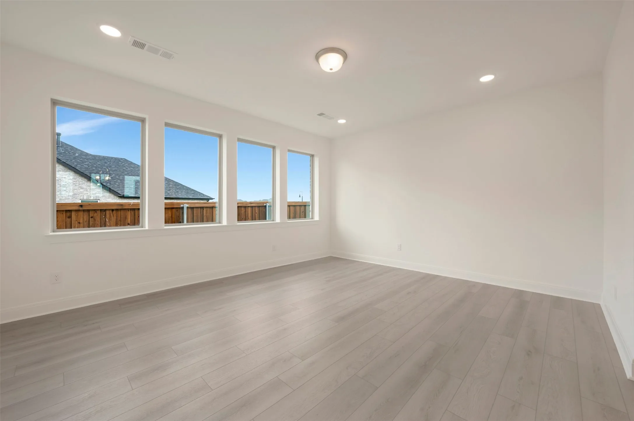 Spacious room featuring four rectangular windows, light wood-finish flooring, recessed lighting, and a neutral white wall finish