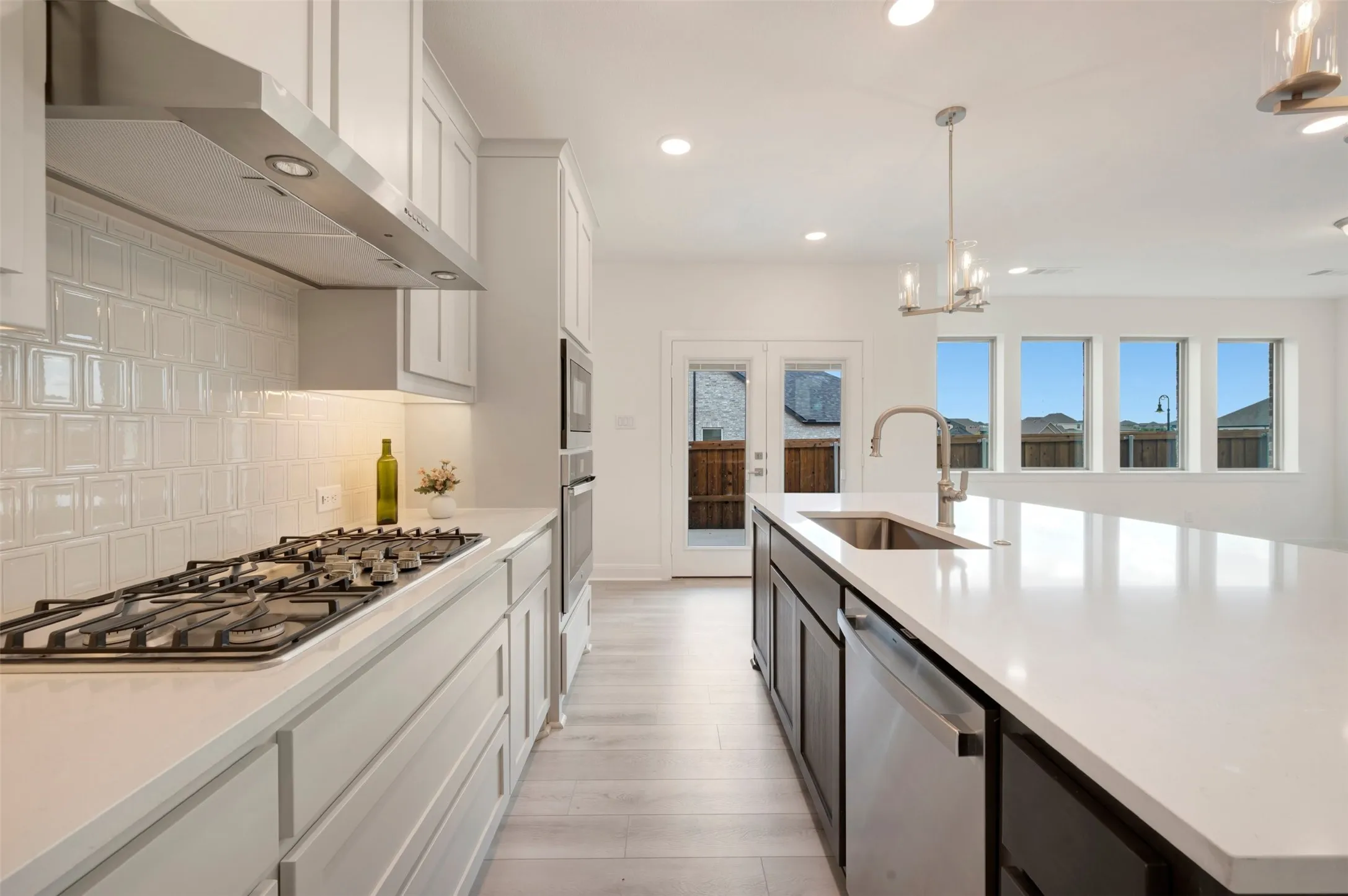 Gourmet kitchen featuring a gas range, stainless steel range hood, white shaker cabinetry, white subway tile backsplash, and light wood-finish flooring