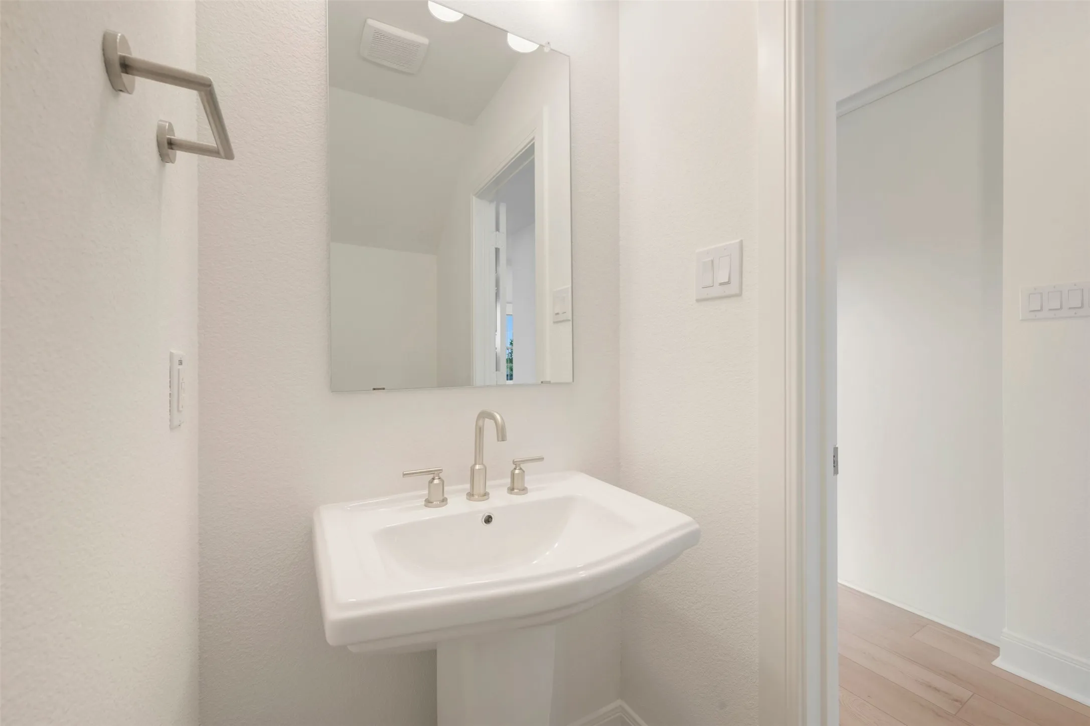 Pedestal sink with brushed nickel faucet, wall-mounted mirror, and vanity lighting