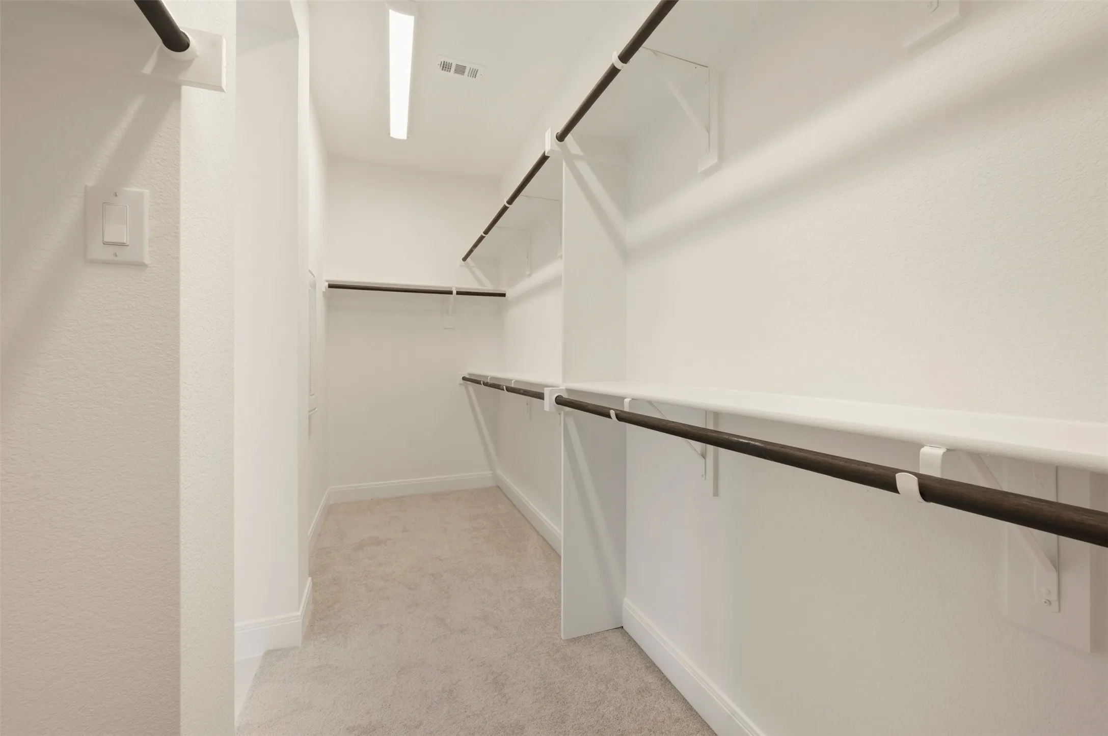 Walk-in closet featuring light beige carpet, white walls, and built-in shelving with dark-toned hanging rods