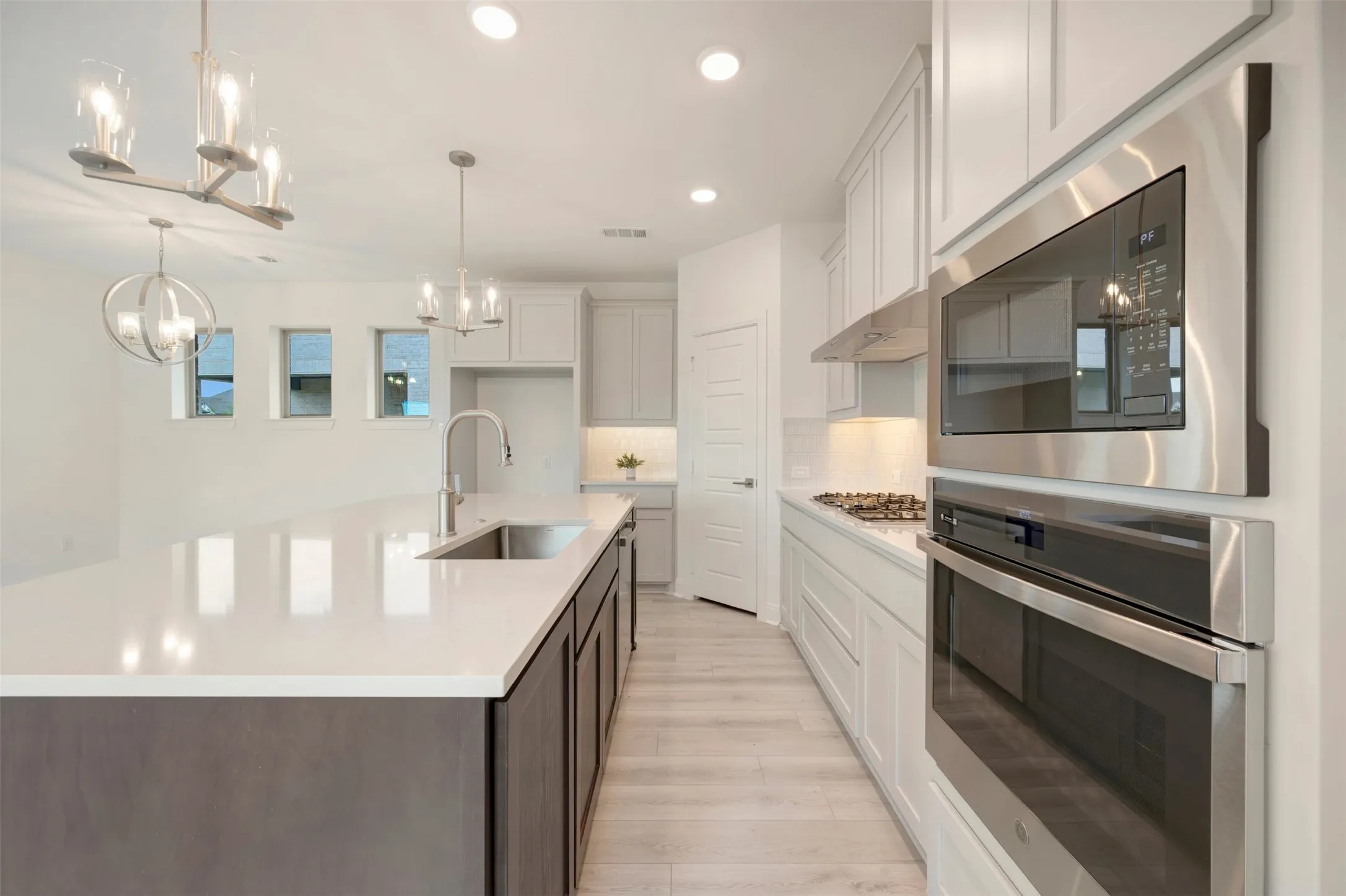 Contemporary kitchen featuring an oversized island with an undermount sink, stainless steel appliances, light wood-finish flooring, recessed lighting, and pendant light fixtures