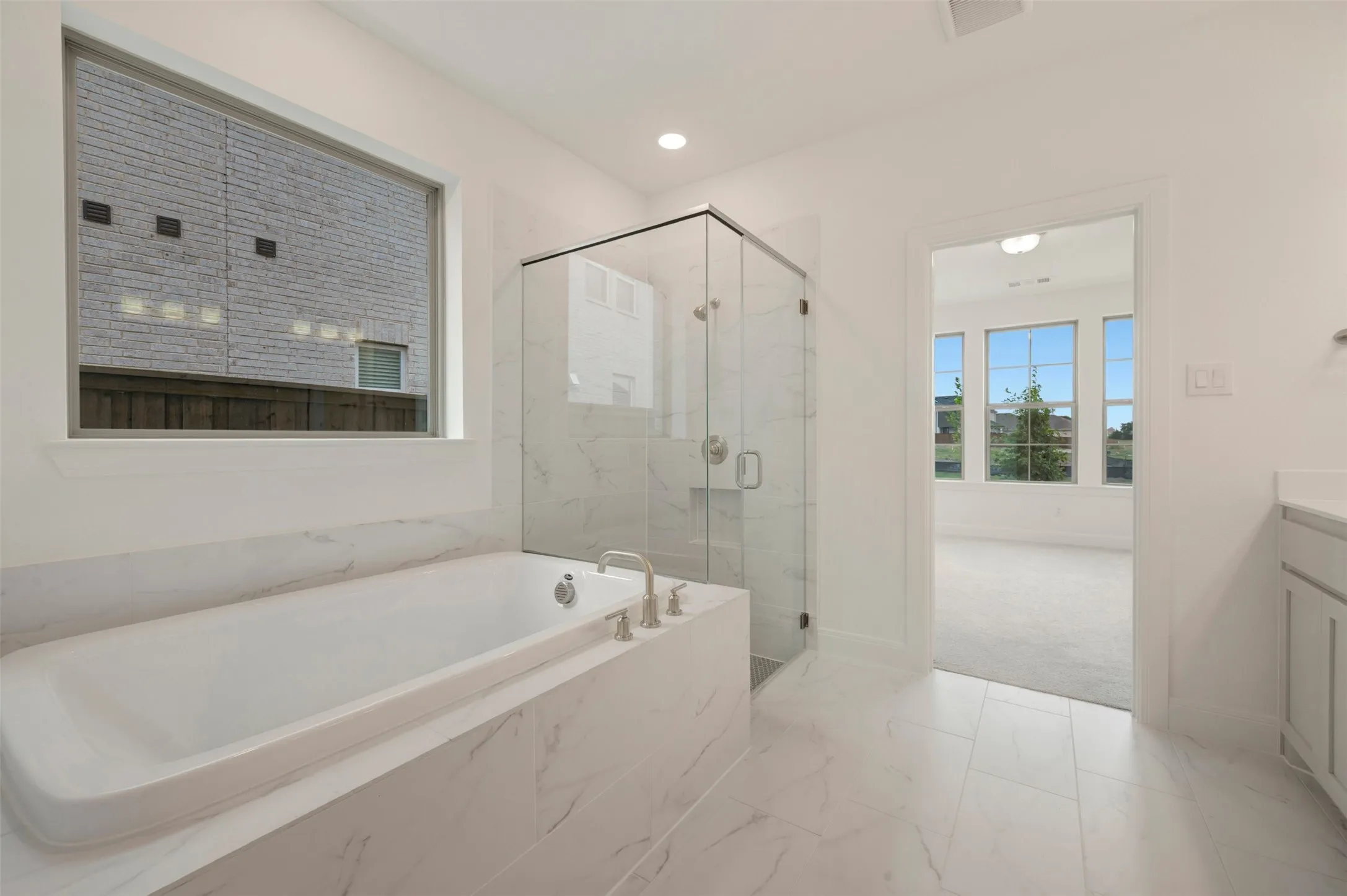Bathroom featuring an expansive soaking tub with brushed nickel fixtures, a glass-enclosed shower with tile surround, and white tile flooring